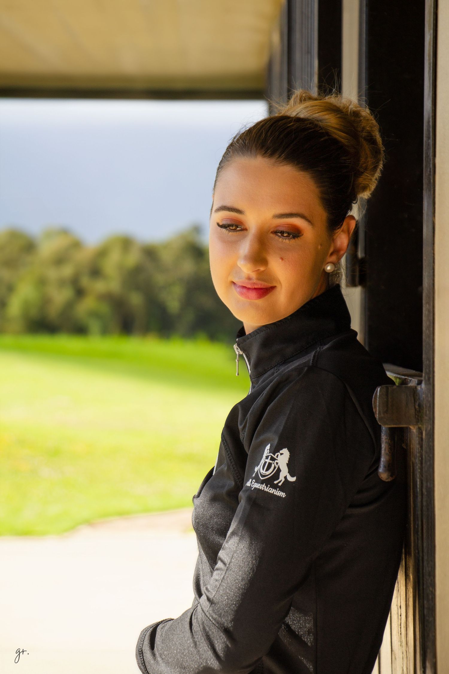 Equestrian apparel showcased in stable doorway with sunny field in background.