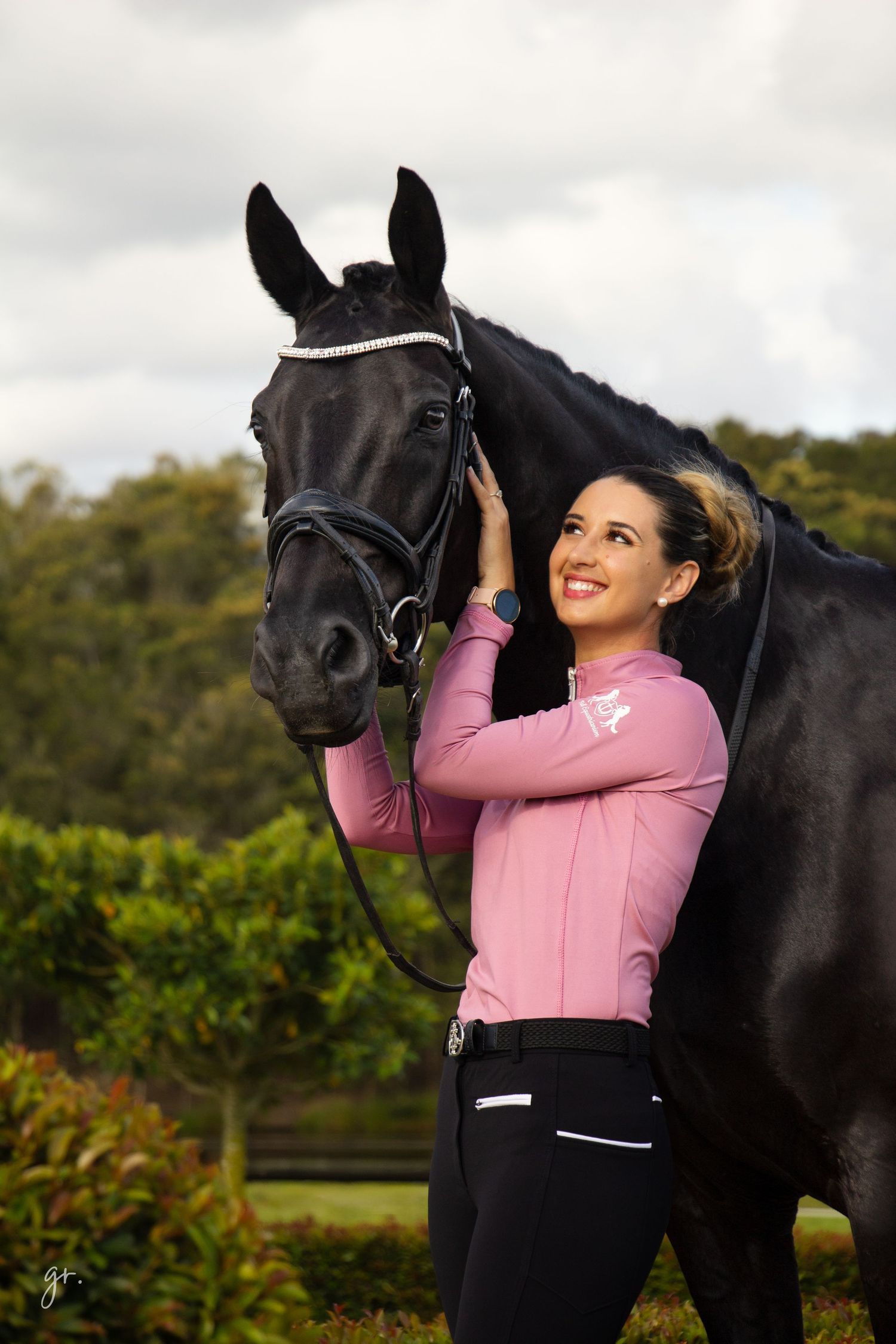 A person in pink athletic wear shares a tender moment with a black horse in an outdoor setting.
