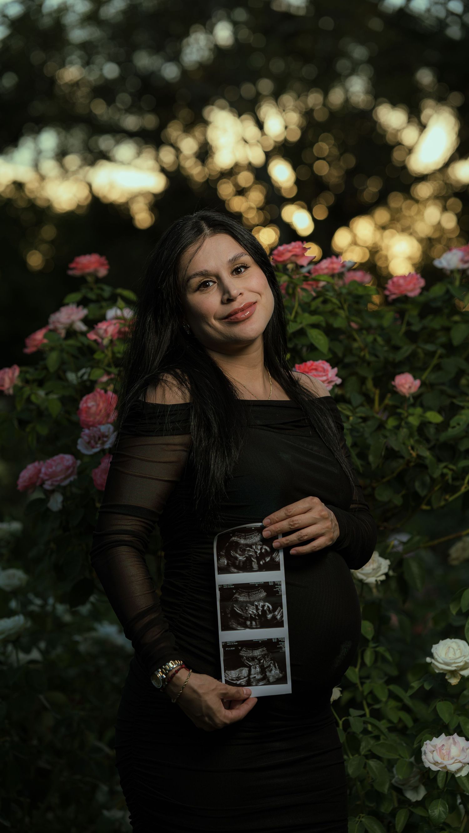A maternity photoshoot in a rose garden at sunset featuring an ultrasound photo display.