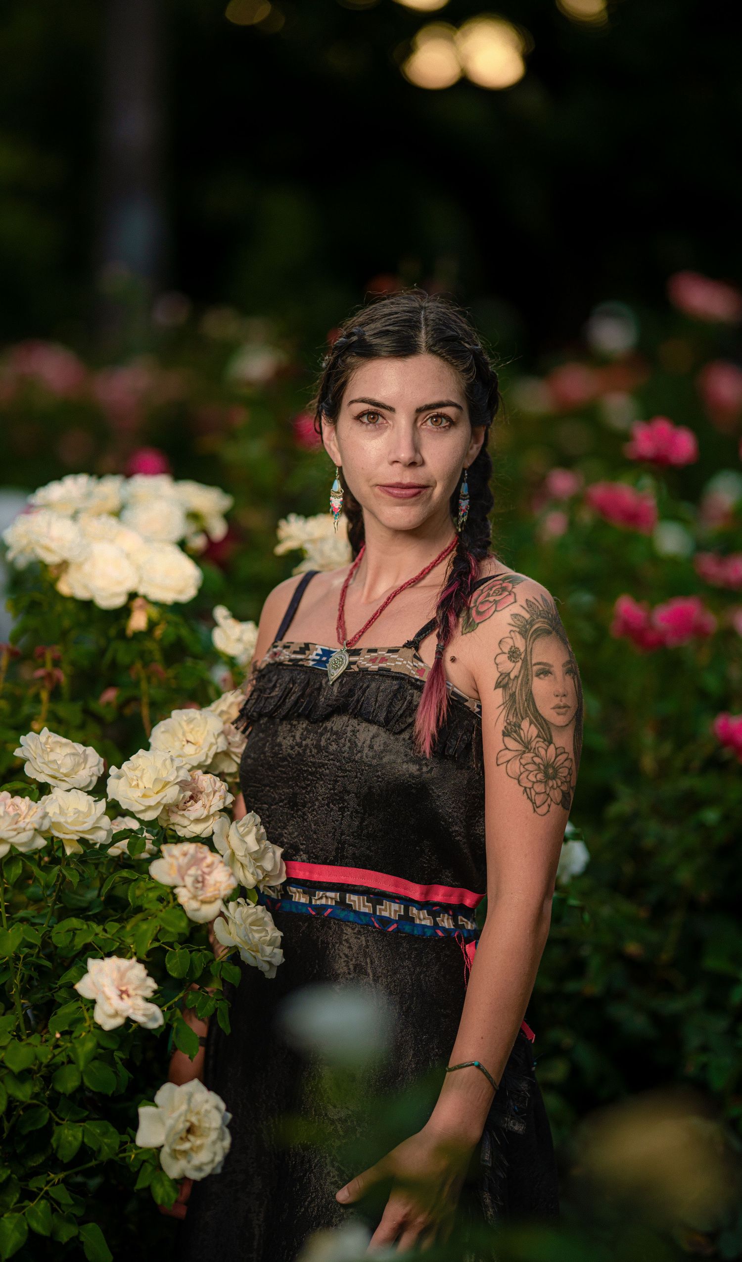 A portrait in a rose garden featuring a black dress with traditional design elements and red trim.