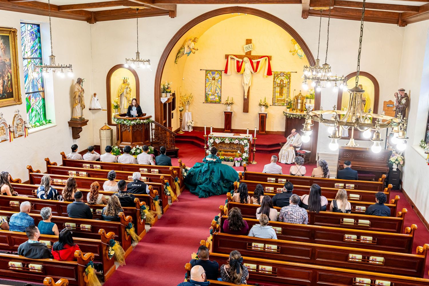 Interior of a Catholic church with wooden pews, arched ceilings, and stained glass windows during a ceremony.