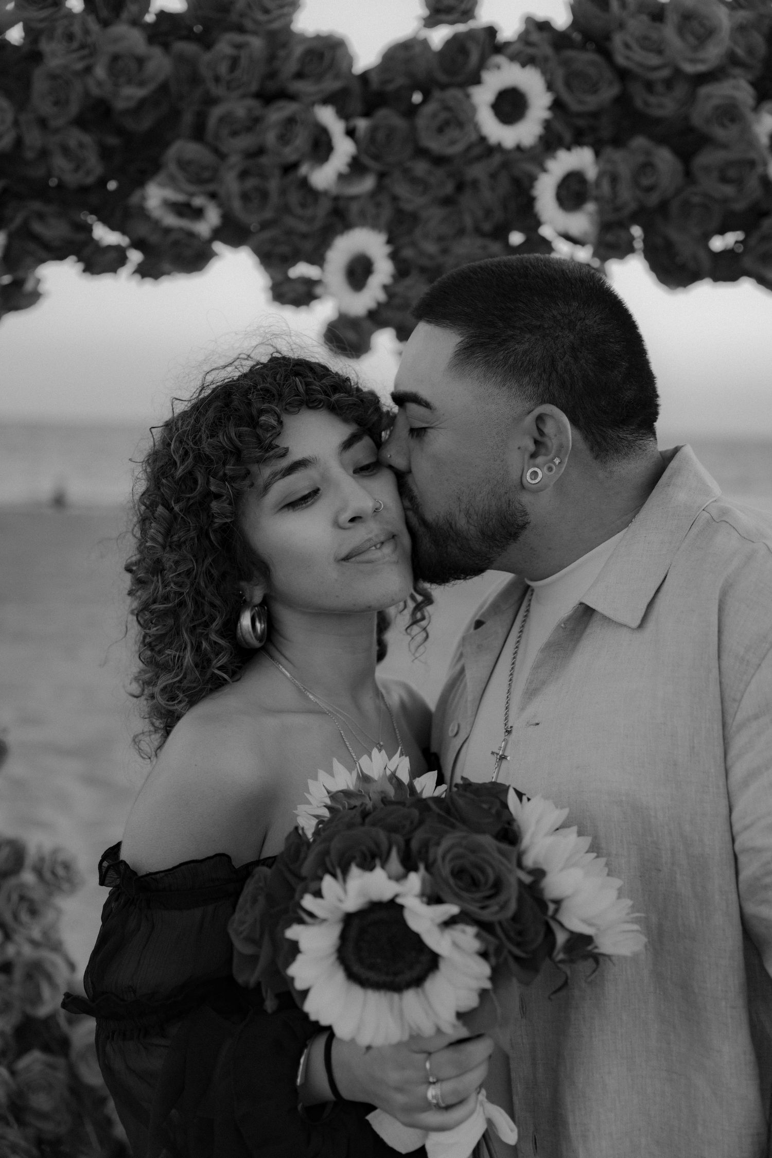A romantic black and white photo series showing a couple embracing with sunflowers against a soft outdoor backdrop.