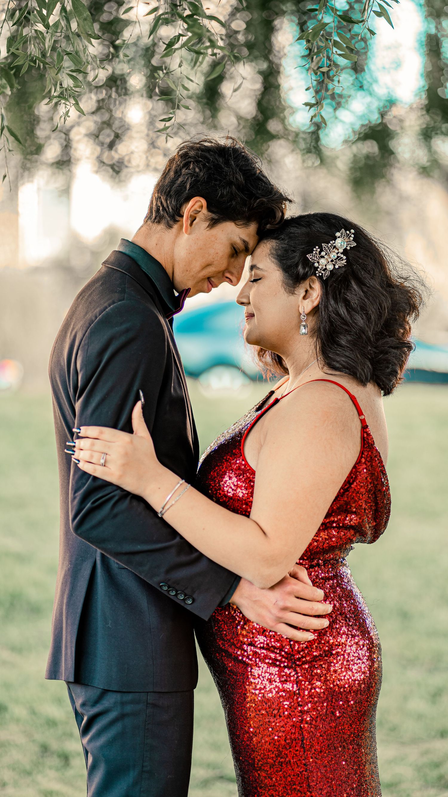 Couple in formal wear sharing an intimate moment outdoors, with the woman wearing a sparkling red dress.