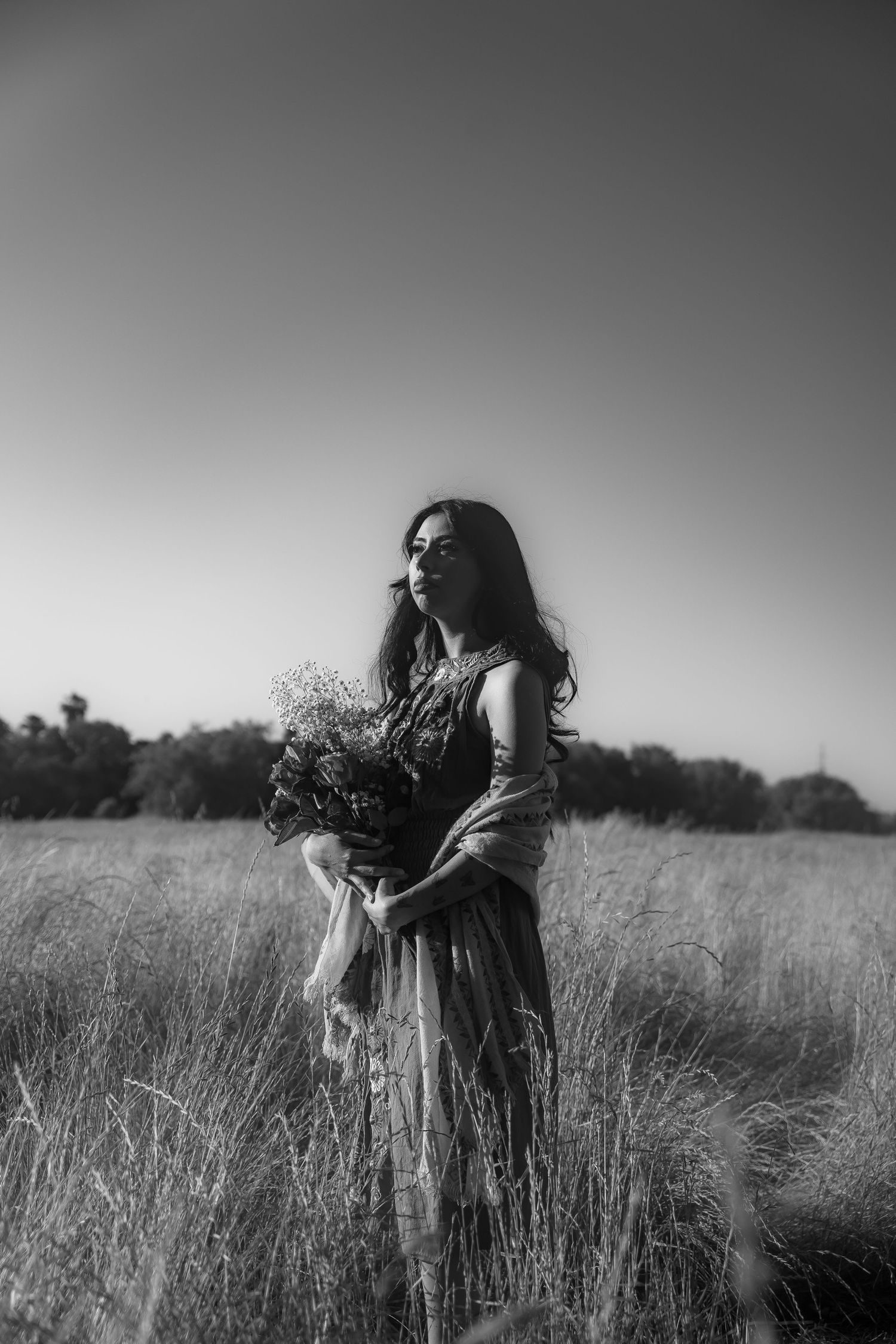 A black and white triptych shows a figure in a flowing dress moving gracefully through a grassy meadow at sunset.