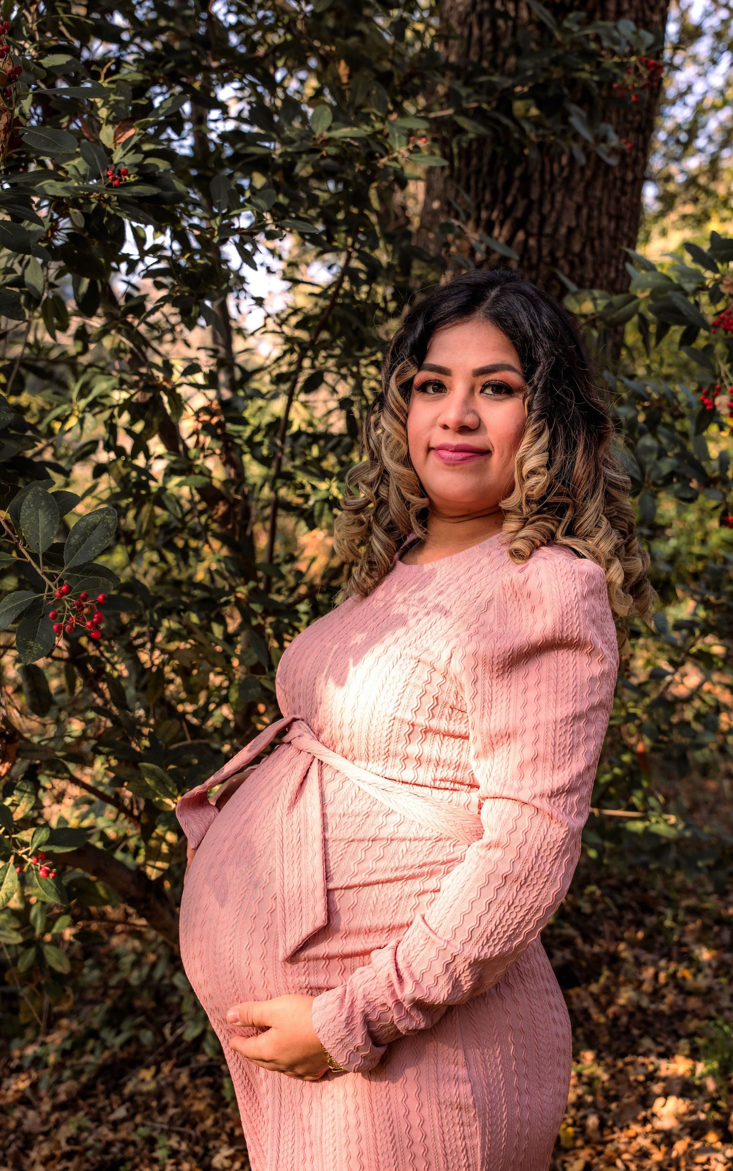 Person in pink sweater poses in natural autumn setting with golden sunlight.