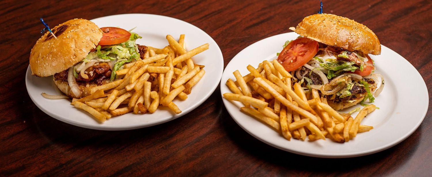 Multiple plates of burgers and french fries arranged on wooden table.