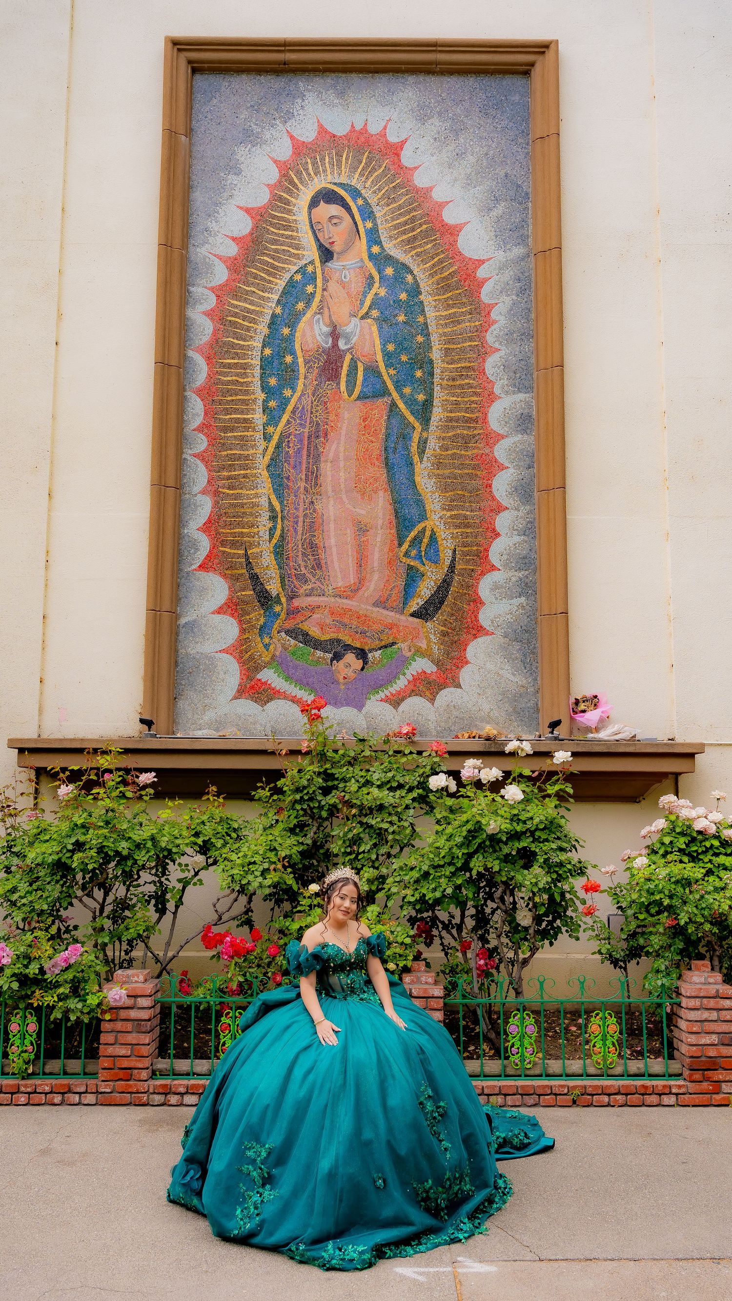 Religious artwork featuring Our Lady of Guadalupe displayed outside with teal formal dress in foreground.