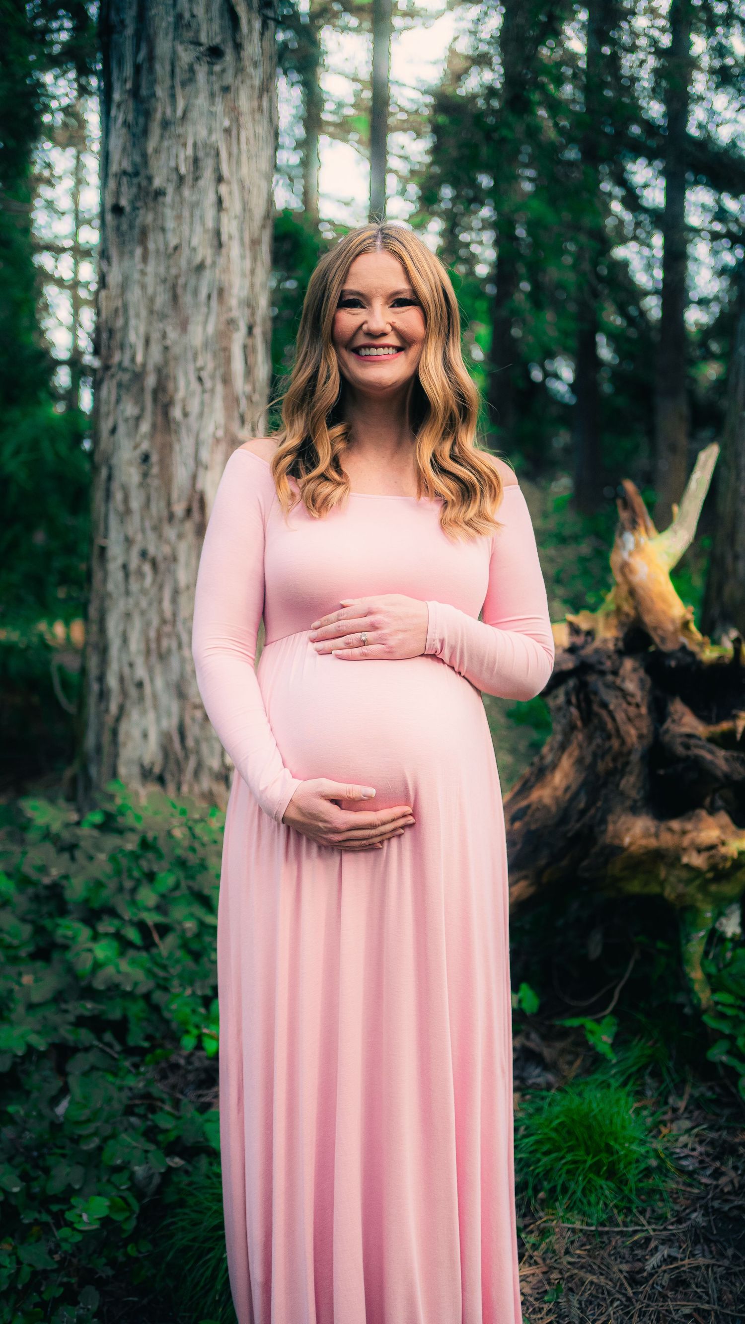 Pink maternity dress photoshoot in a lush forest setting with tall trees.