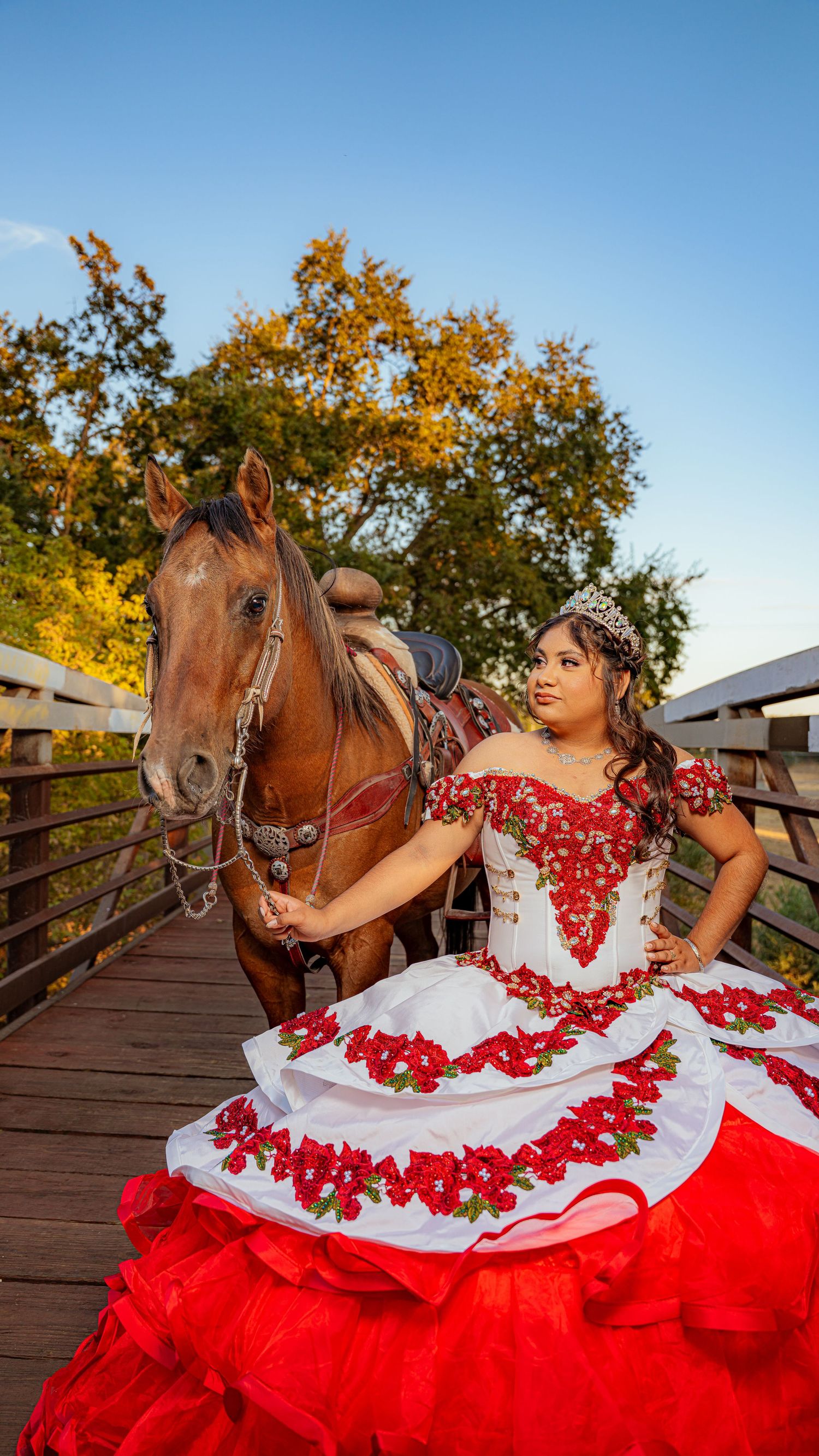 Traditional red and white Mexican dress photographed with horse on wooden bridge.
