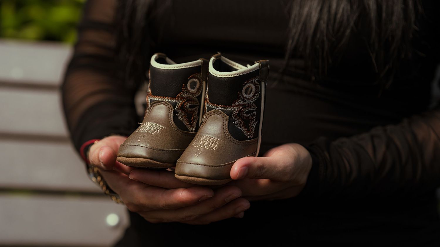 Close-up of hands holding small brown leather baby boots.