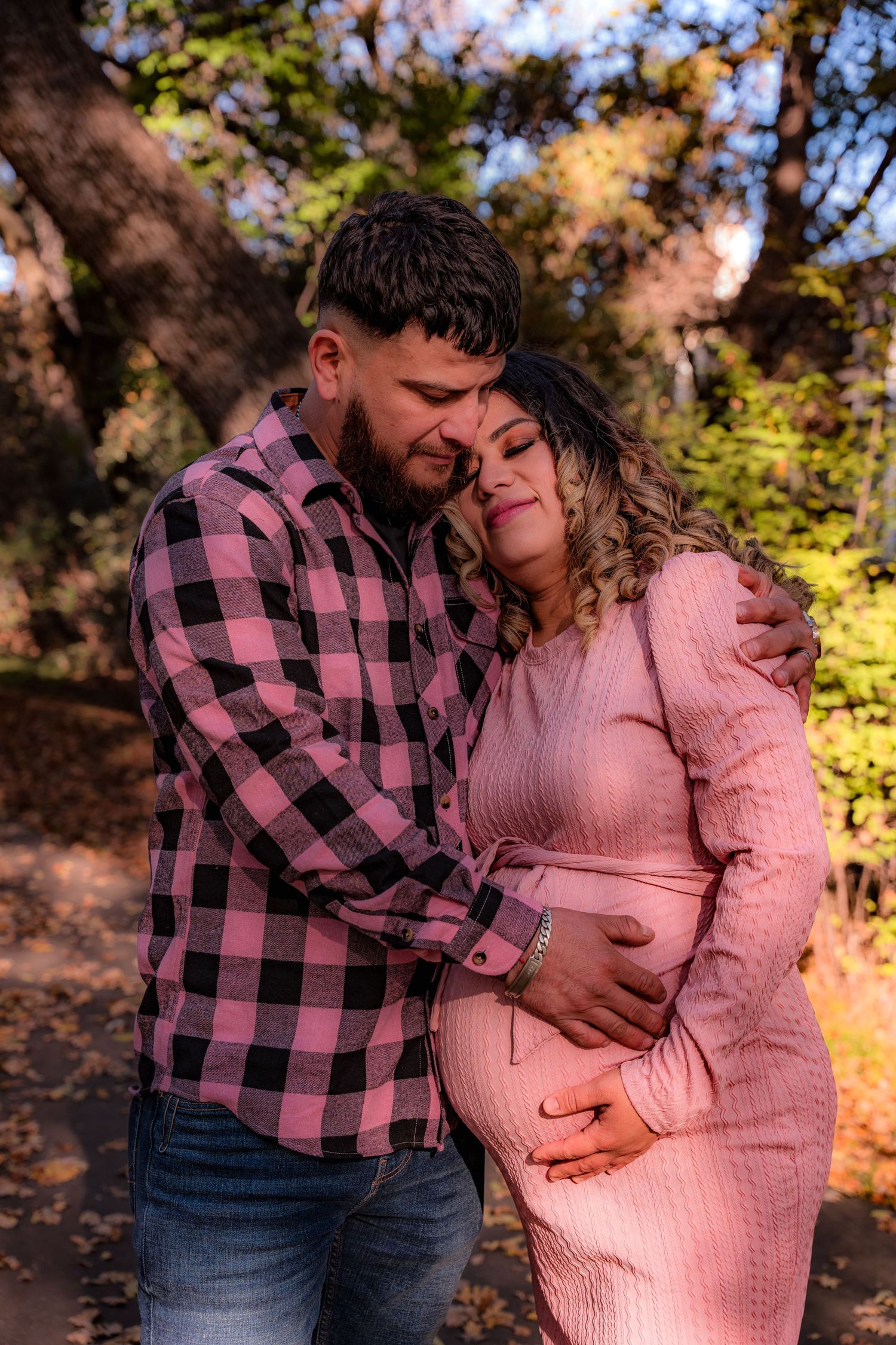 Couple shares tender moment in autumn setting with pink sweater and plaid shirt.