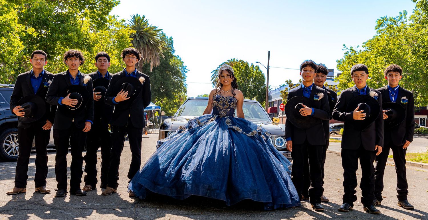 A group in formal attire poses outdoors for a quinceañera celebration photo.