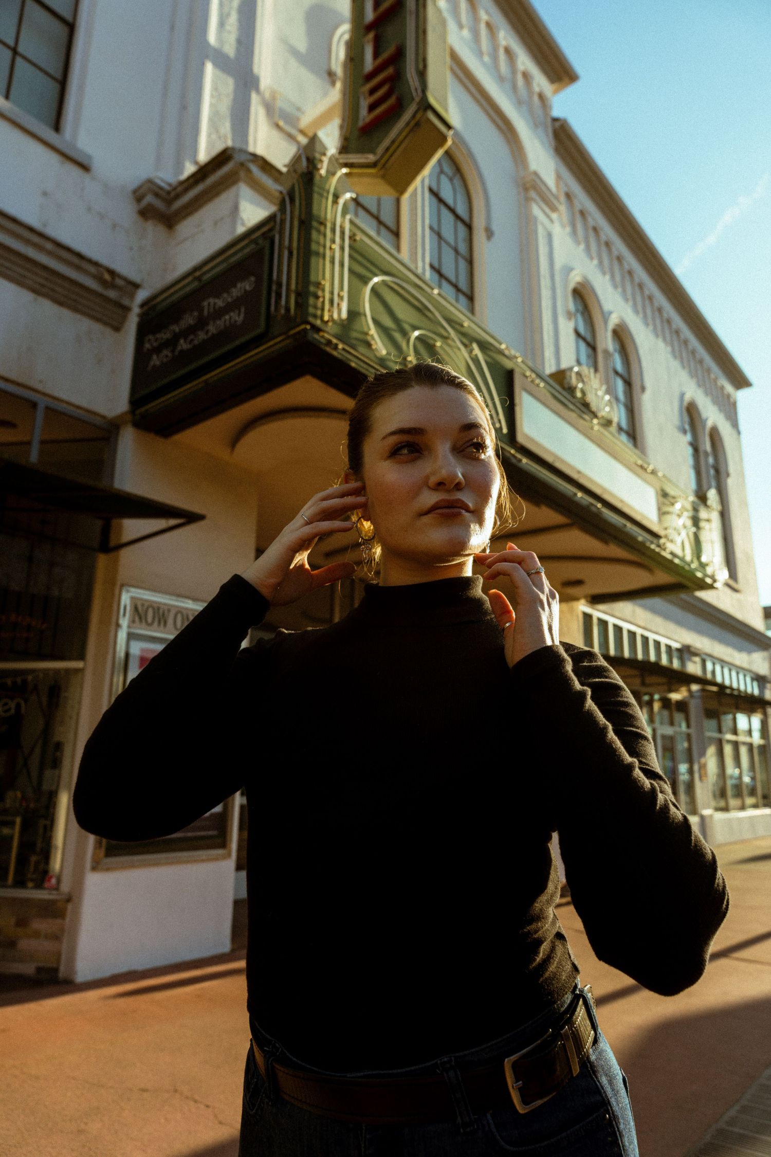 A fashion portrait in front of a vintage storefront featuring a black turtleneck sweater and casual styling.
