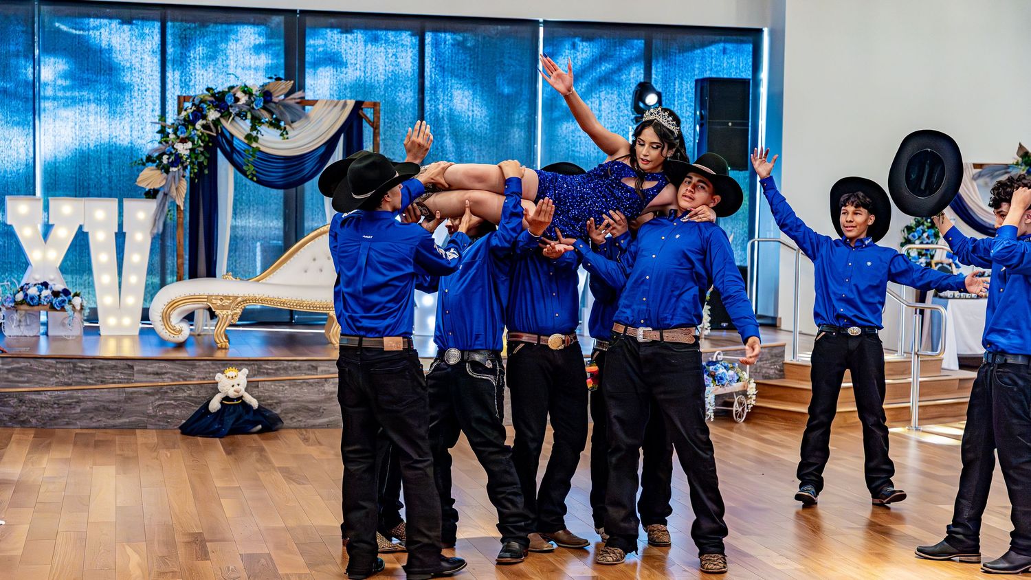 Wide angle shot of dancers in blue uniforms practicing in a bright dance studio.