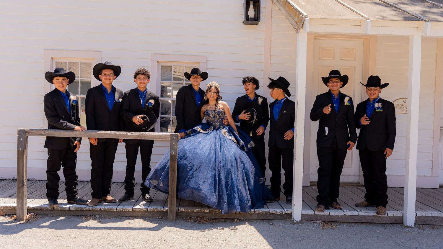 A group dressed in cowboy hats and formal wear stands under an outdoor pavilion.