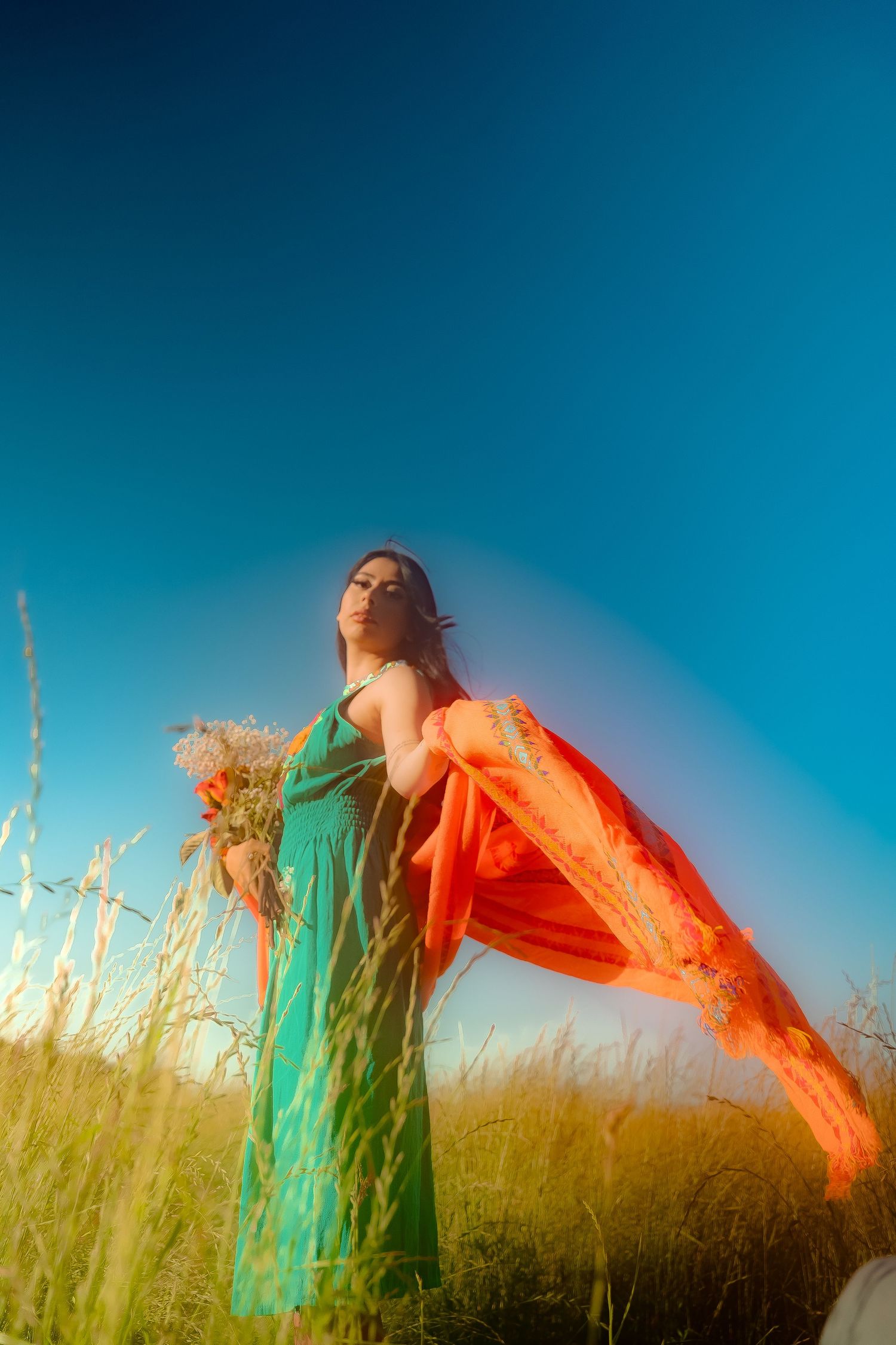 Ethereal scene of billowing orange and turquoise fabric dancing in a golden field at sunset.