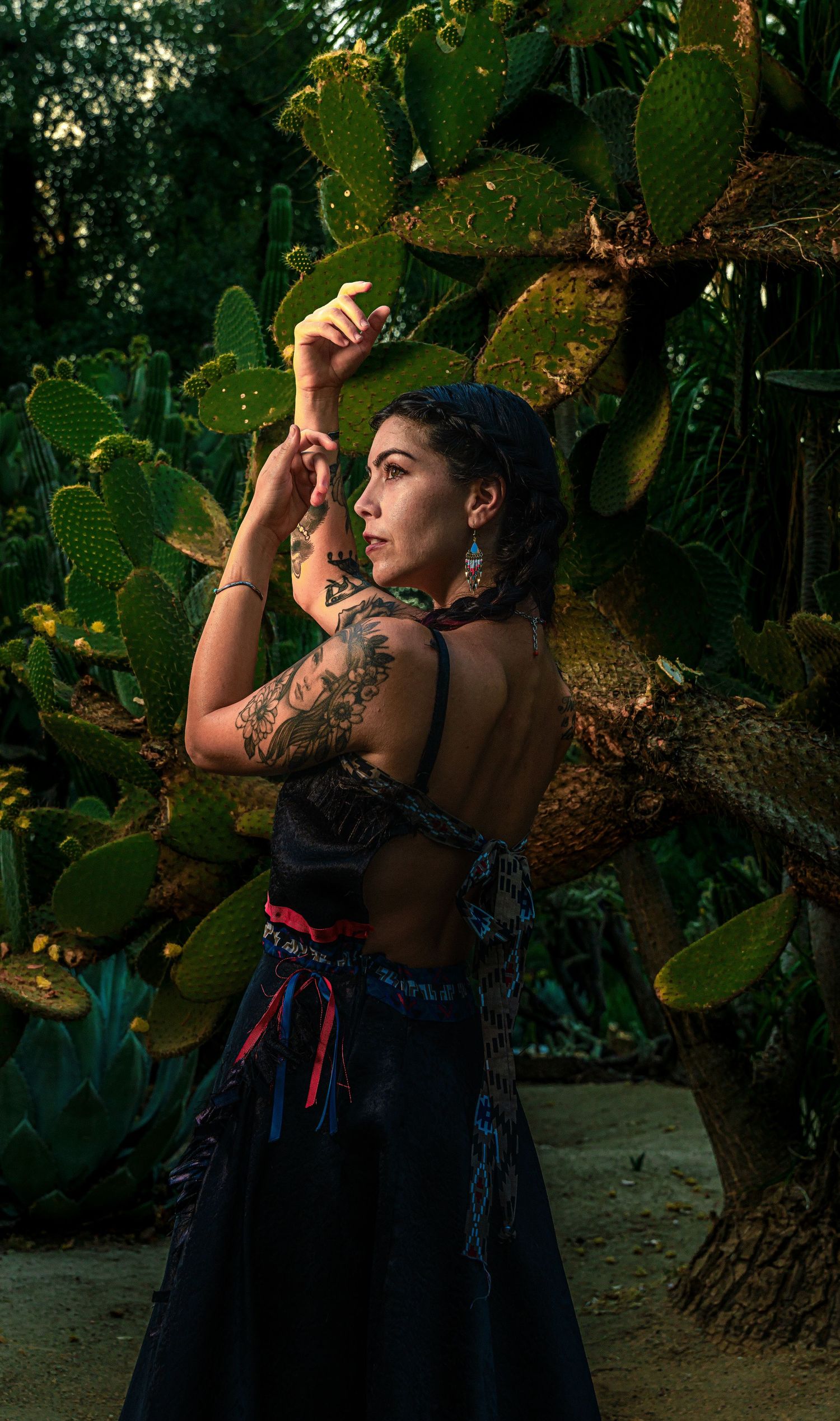 A person in a navy blue dress poses against a backdrop of lush green cactus plants in a garden setting.