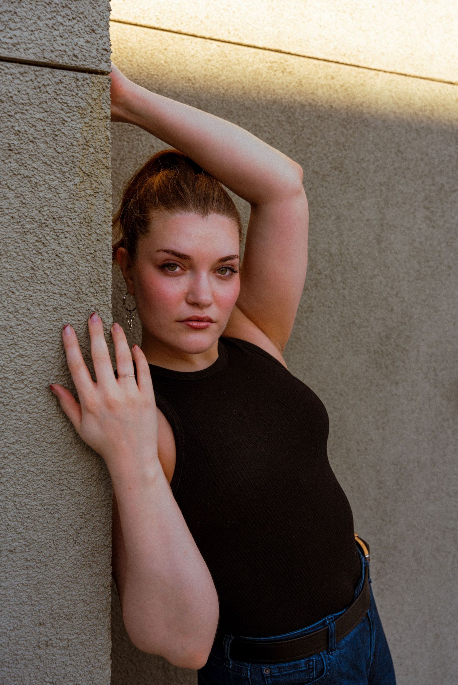 A series of fashion portraits showing someone in a black top and jeans posing against a textured wall.