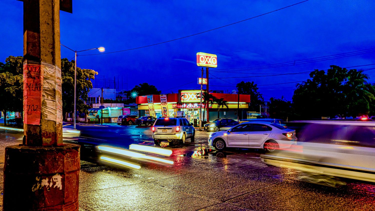 A panoramic cityscape at dusk with streaking car lights and illuminated buildings along a busy street.