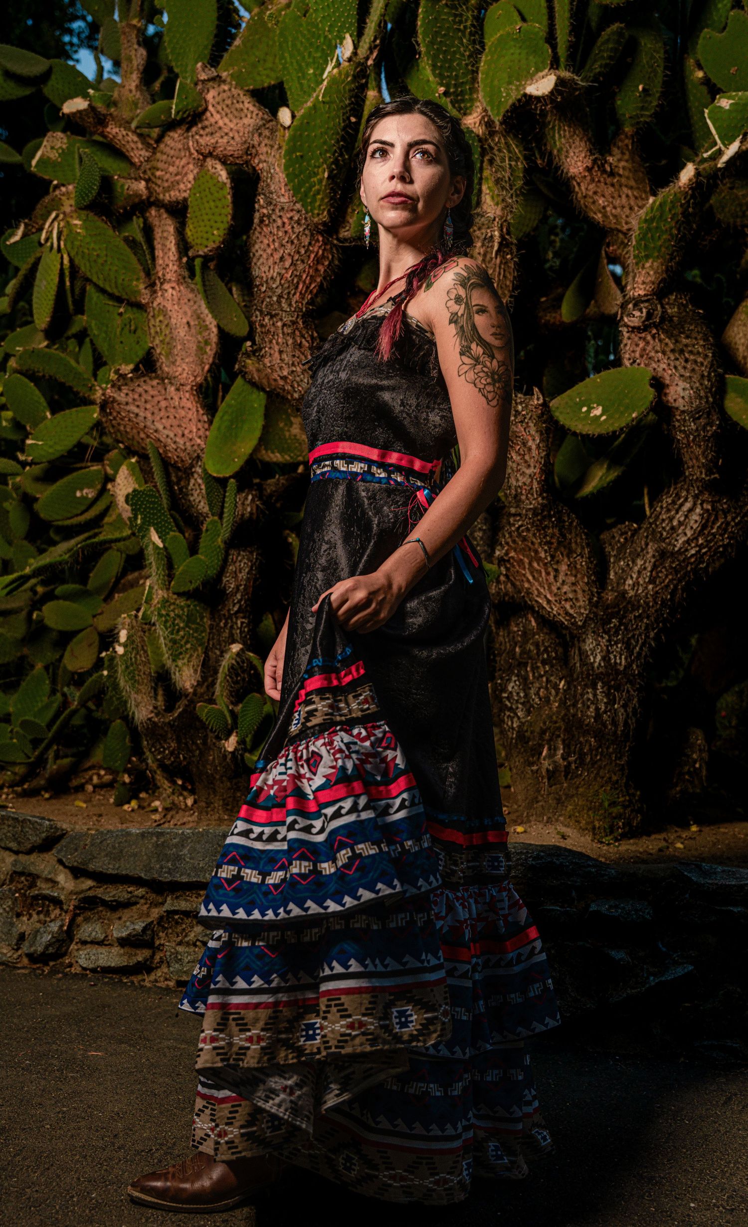 A black dress with colorful ruffled tiers stands out against a backdrop of cactus plants in an artistic portrait.