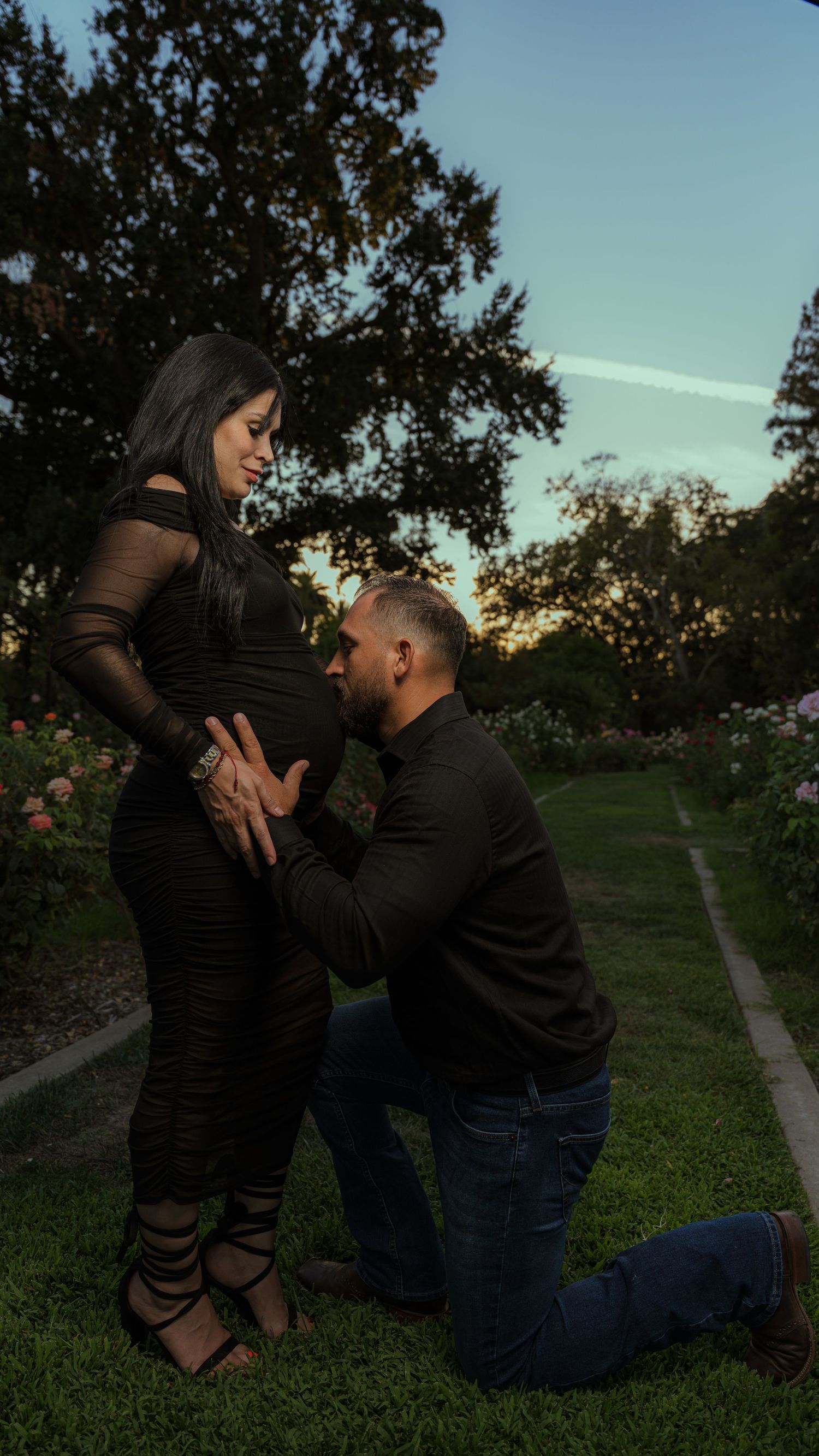 A romantic maternity moment captured in a garden at sunset.