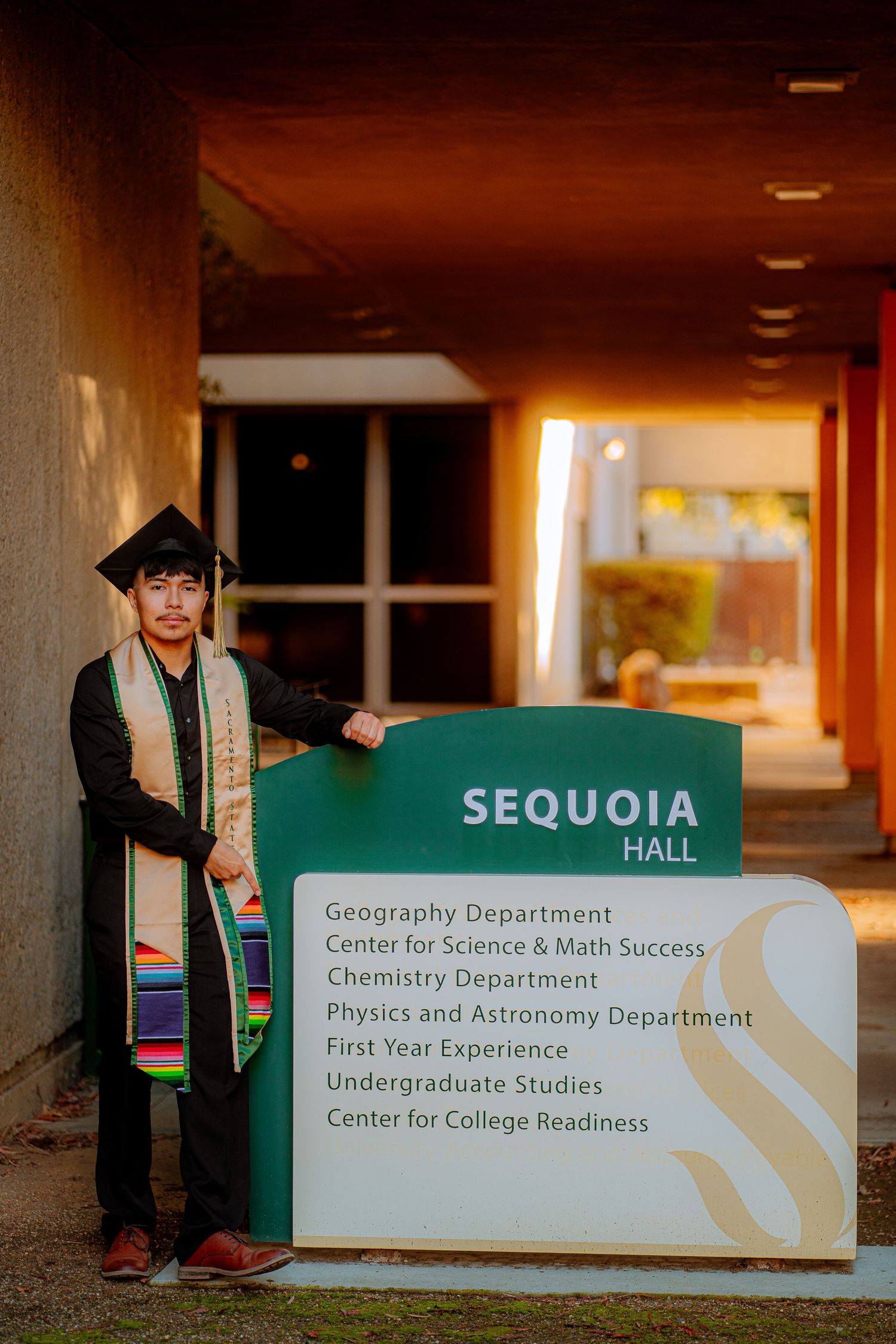 Graduation photos taken in front of Sequoia Hall directory signs at a university.