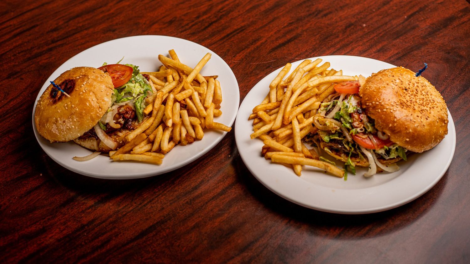 Row of hamburger plates with golden french fries on dark wooden surface.