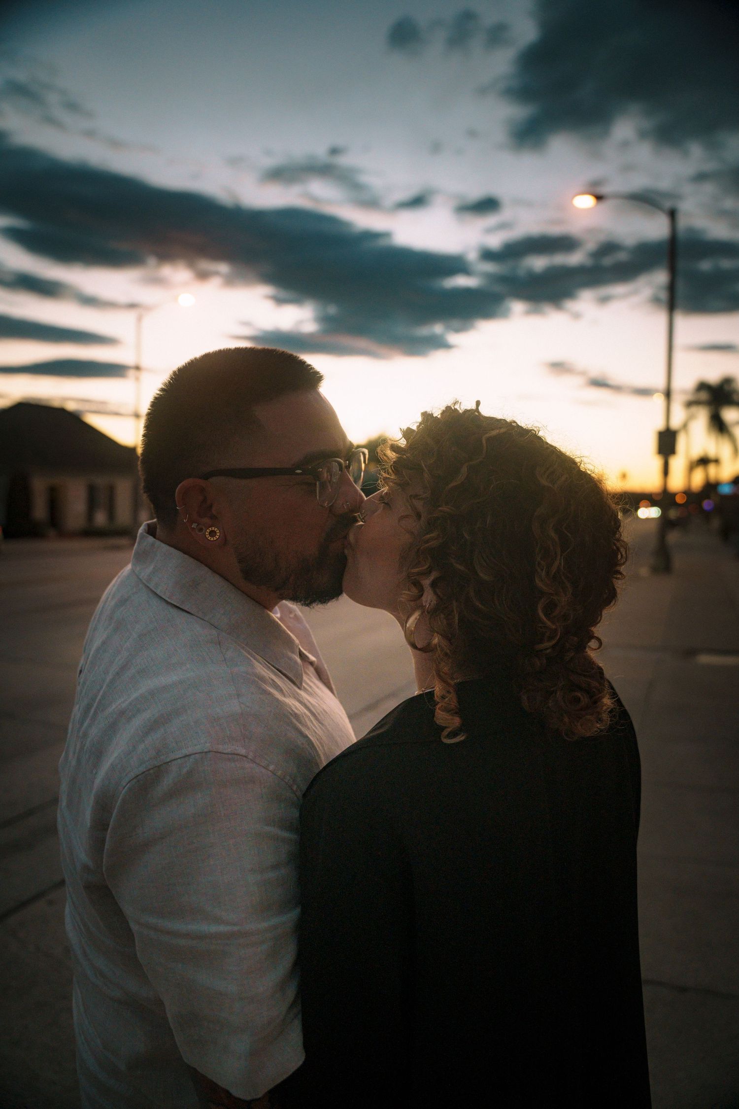 A couple shares an intimate moment at sunset against a dramatic cloudy sky.