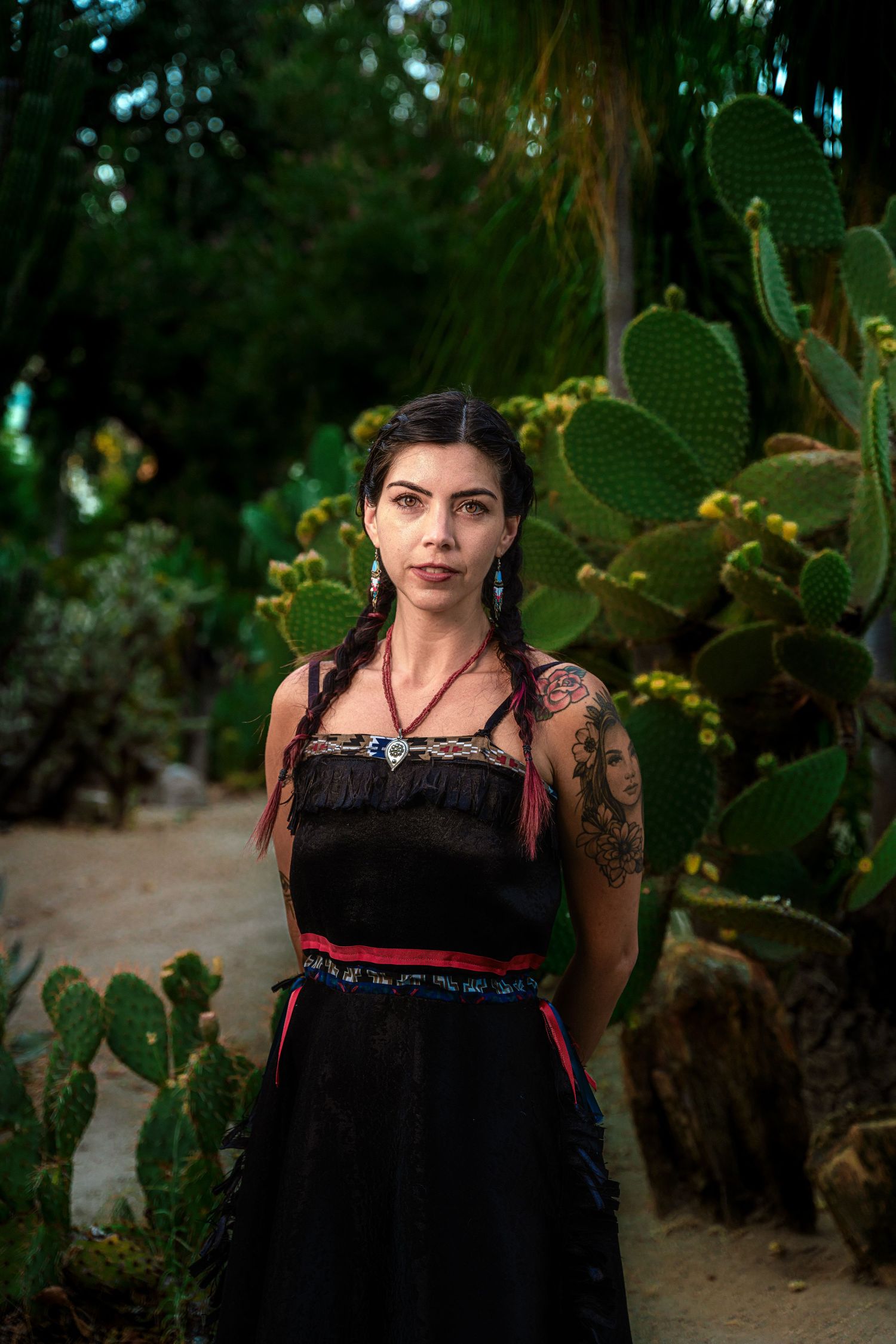 A striking portrait against cacti featuring a black dress with red accents and traditional design elements.