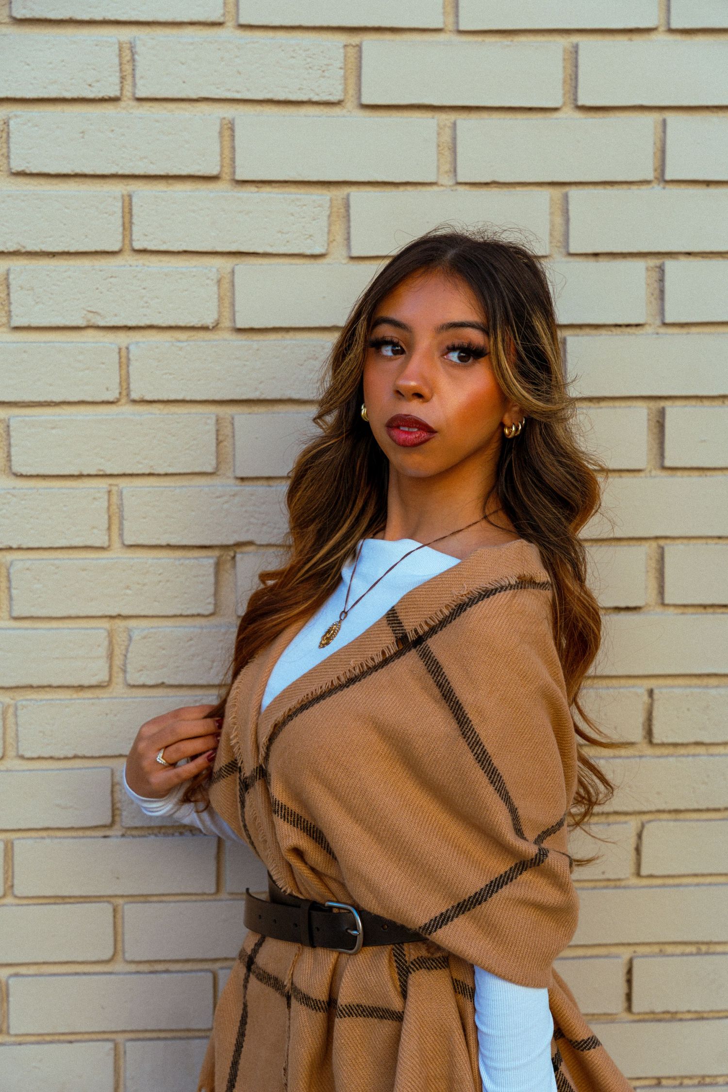 Fashion model poses against brick wall wearing tan coat and white top in dynamic multi-angle photo collage.