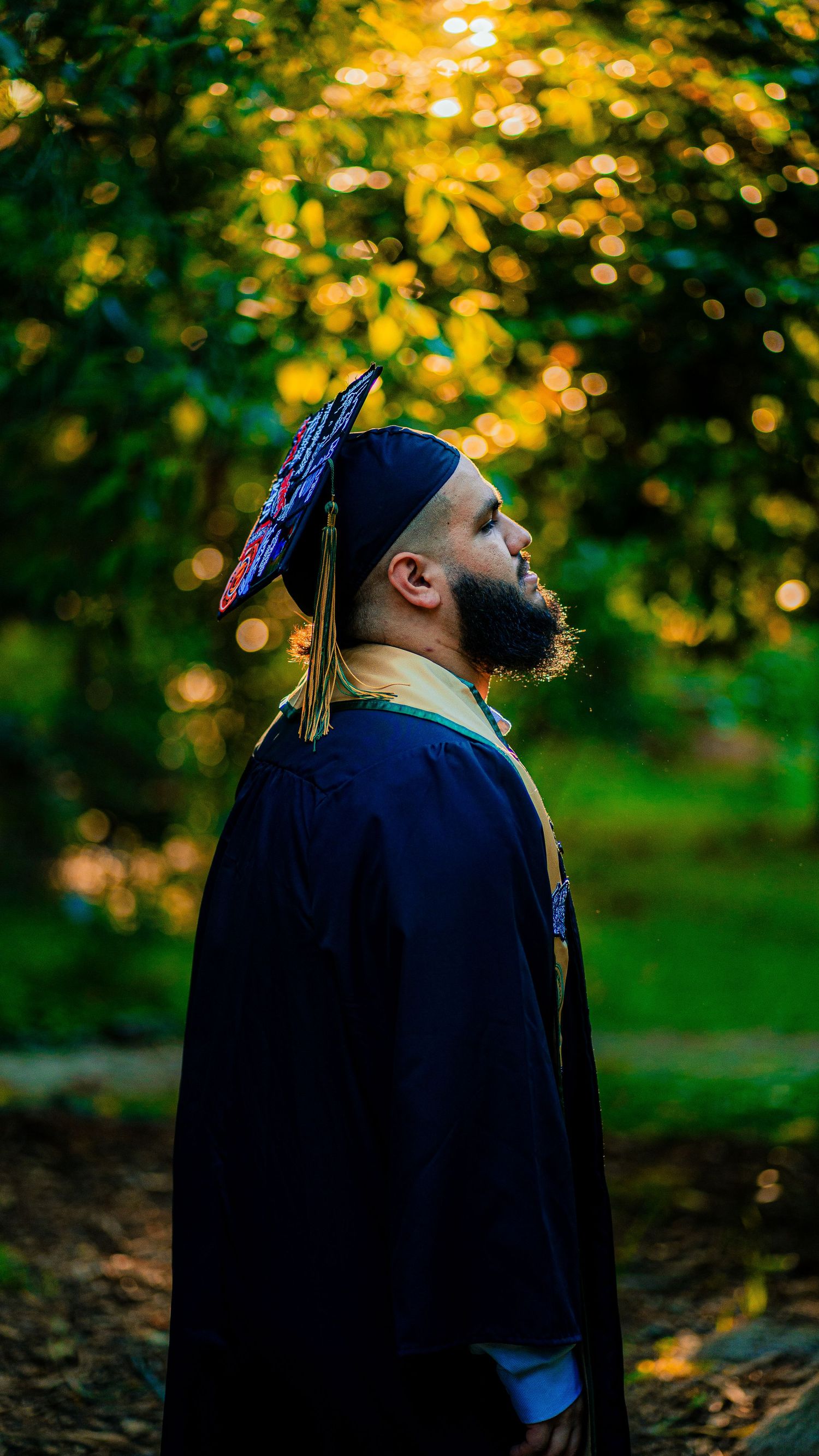 Side profile of graduate in cap and gown against golden sunset bokeh.