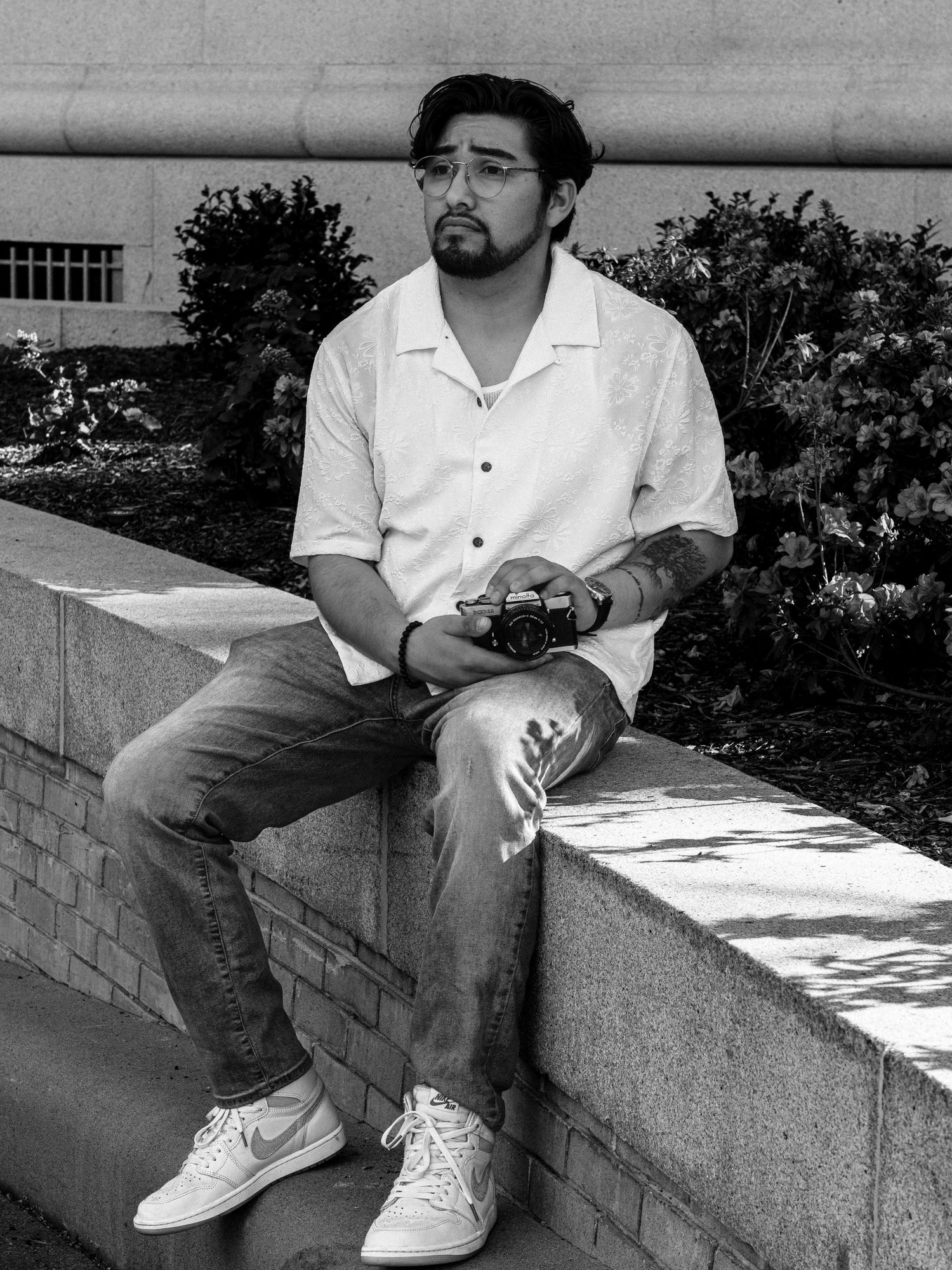 Black and white artistic portrait series showing someone sitting casually on a concrete ledge outdoors.