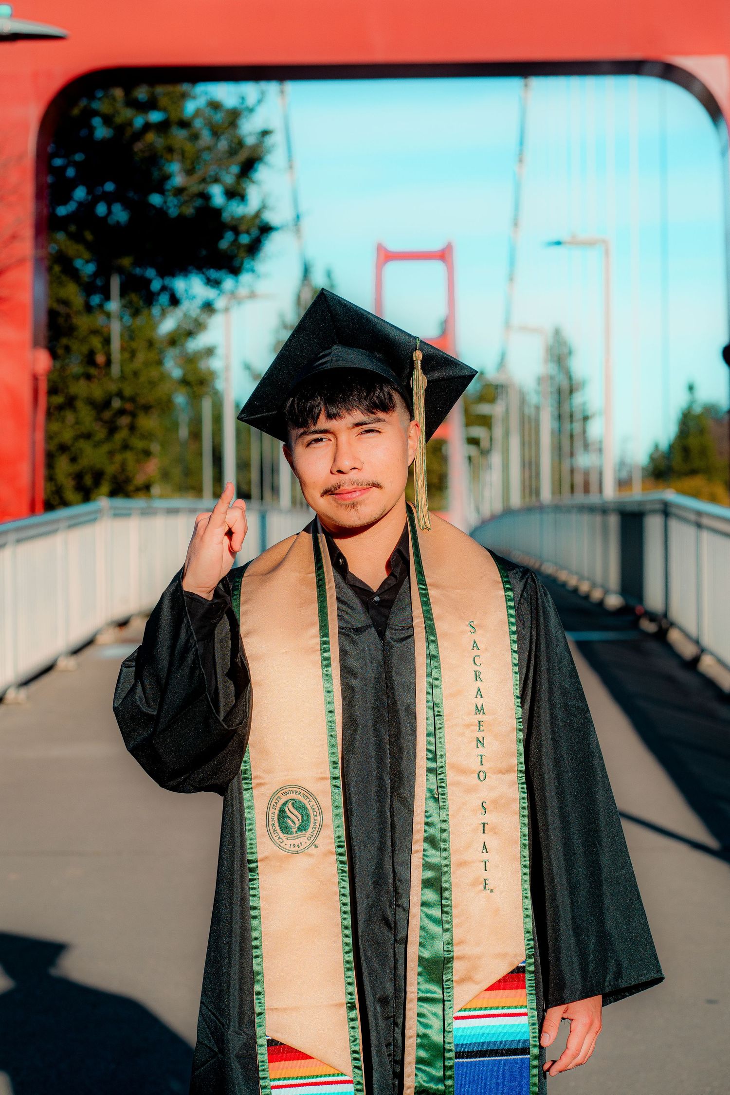 Graduate poses with cap and stole against red urban background.