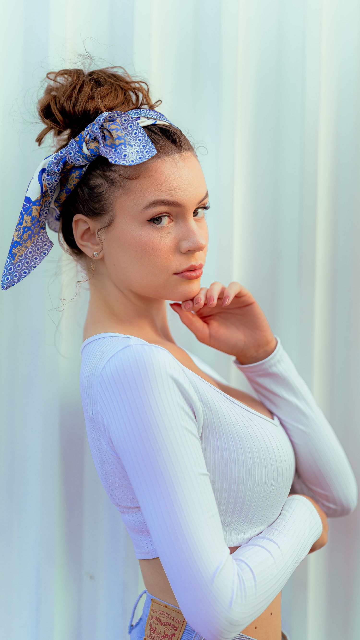 A person in white long sleeves and blue bandana poses thoughtfully against a light background.
