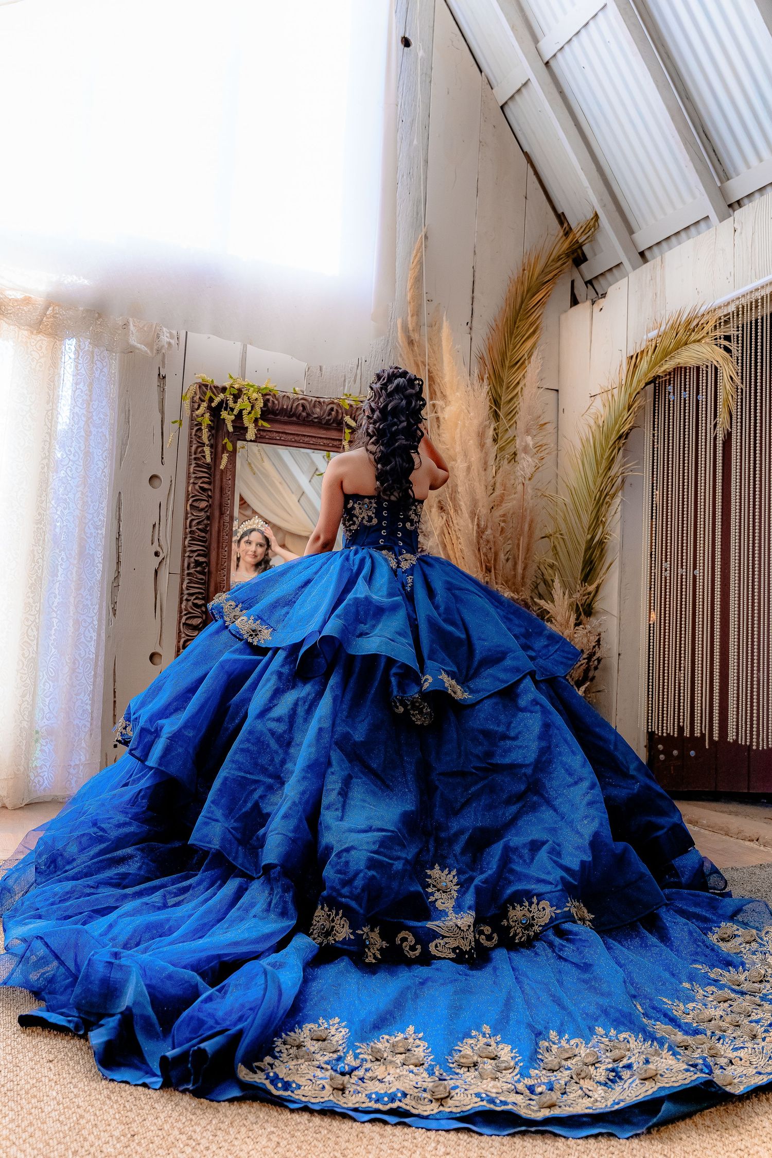 Back view of a dramatic royal blue ballgown with gold embellishments and full layered skirt.