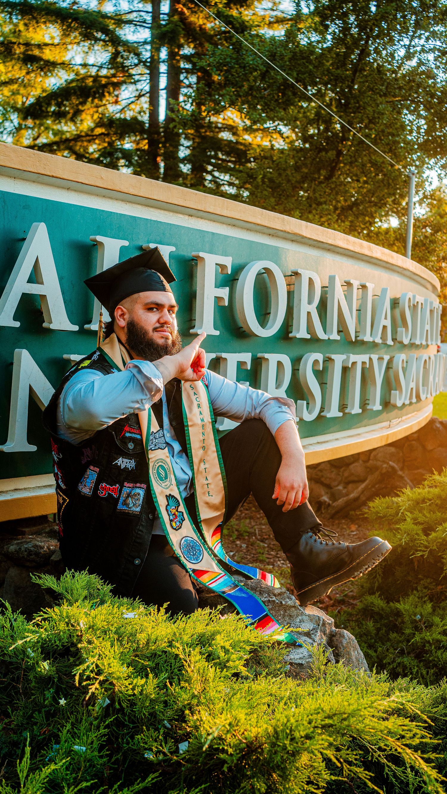 Graduate in regalia poses by California State University sign during golden hour.