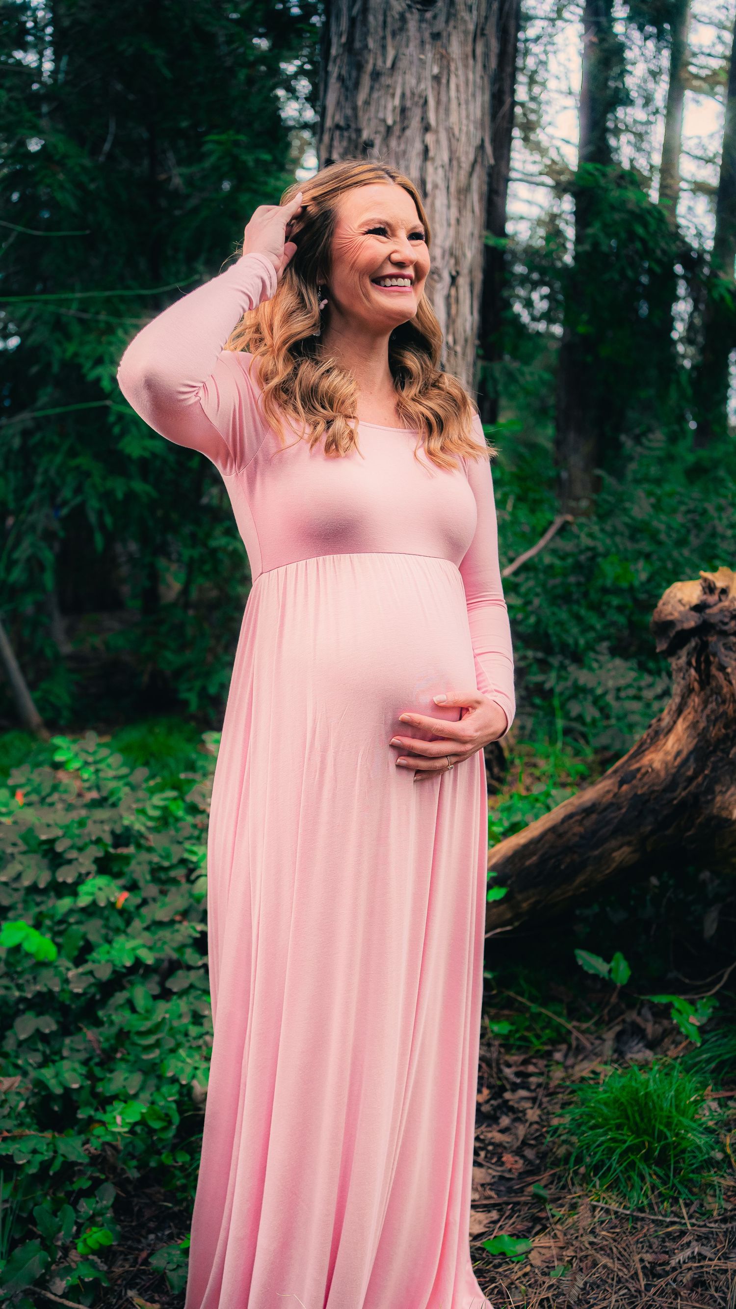 Maternity photography session among tall trees in a green forest setting.