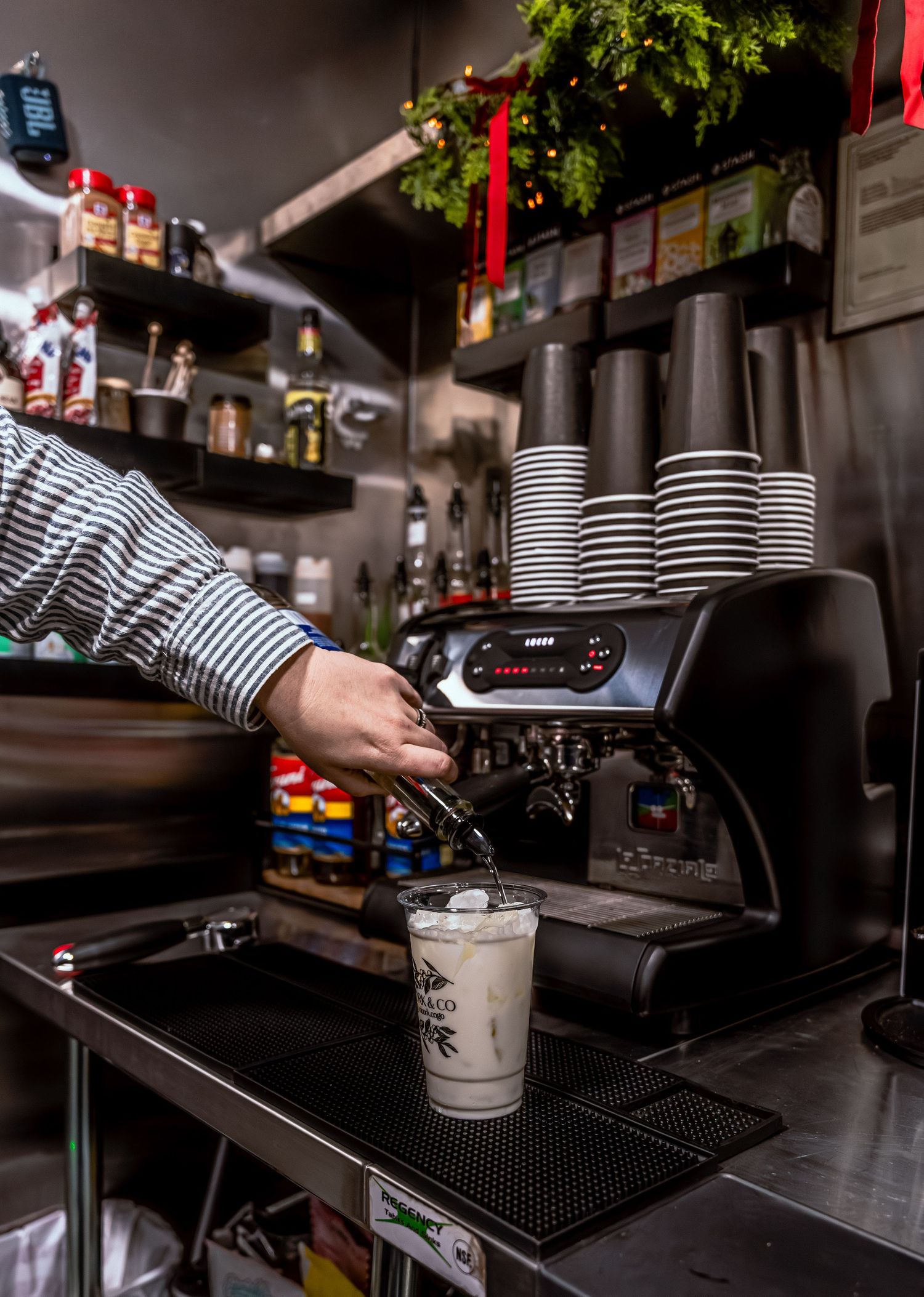 Barista preparing drinks at a coffee bar with equipment and supplies.