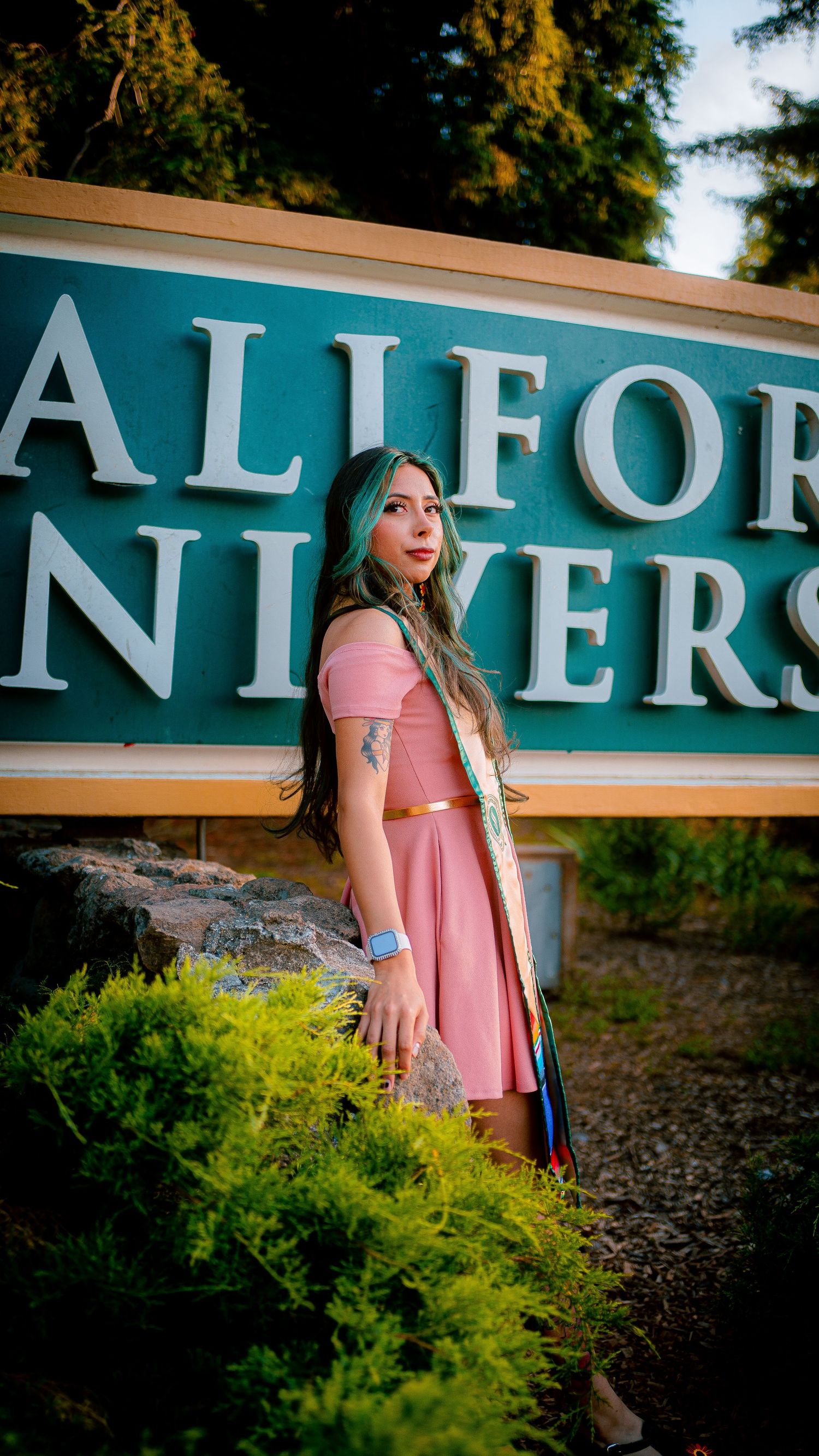 Graduate in pink dress posing near California State University signage.