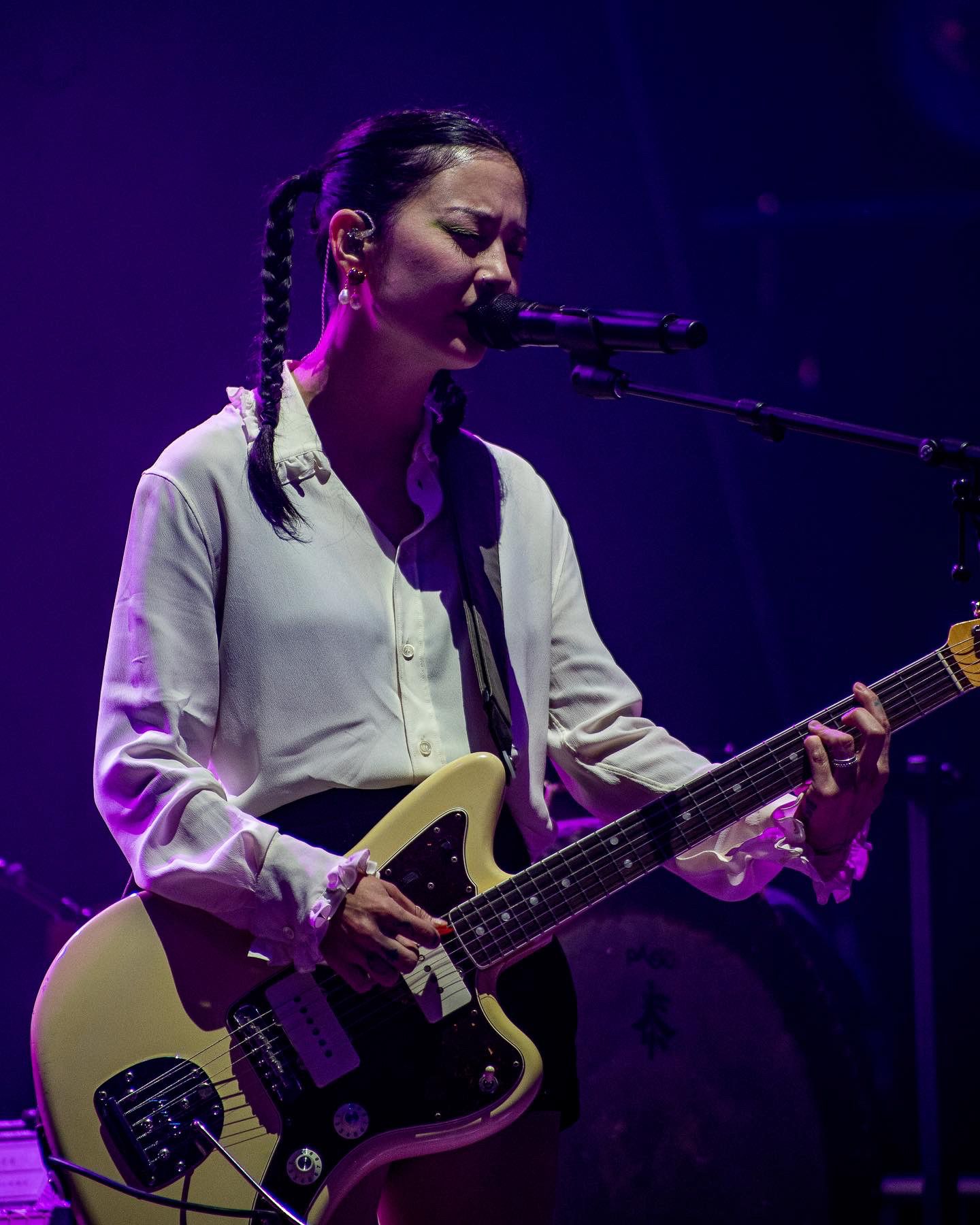 Musician playing bass guitar on stage with purple lighting effects.