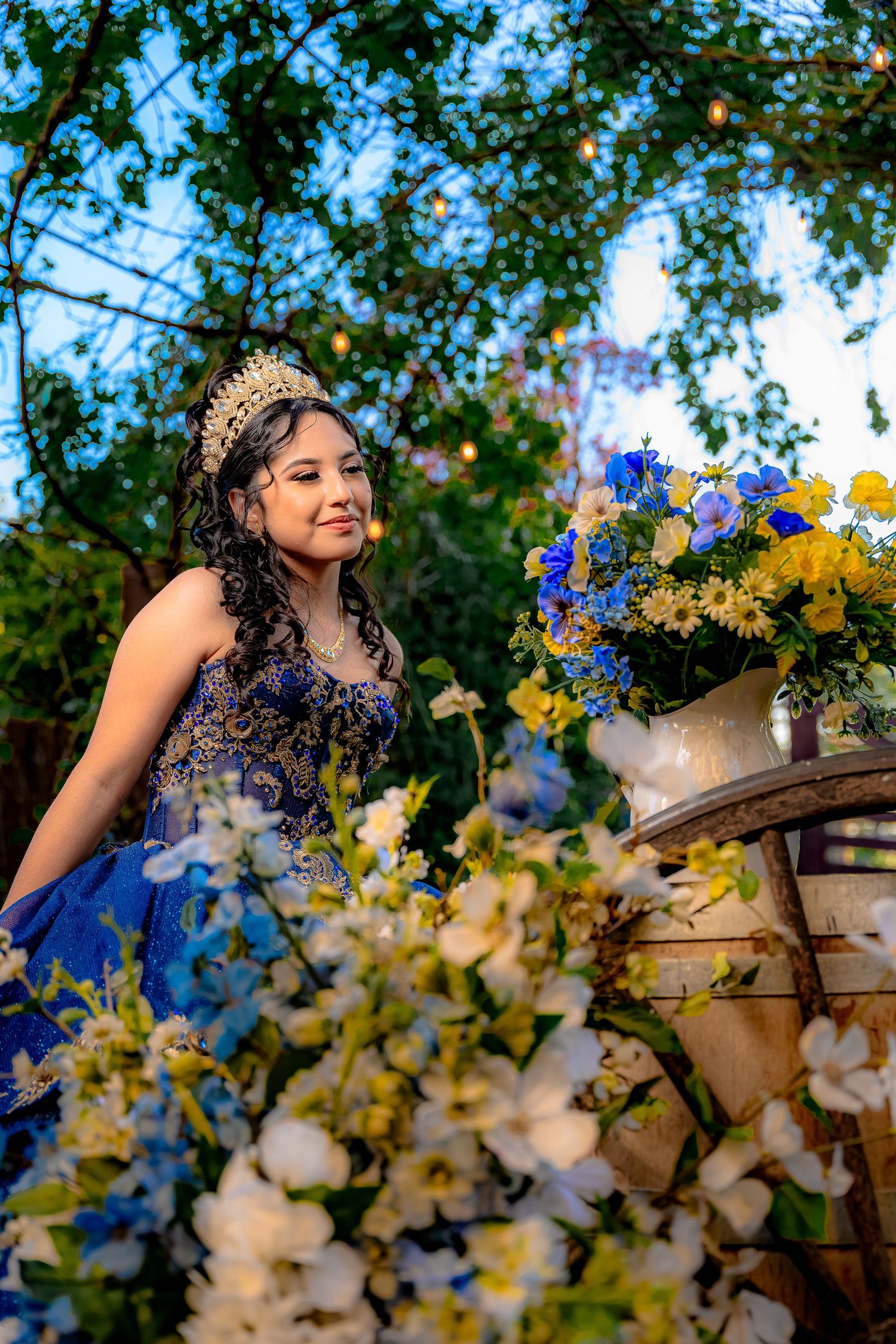 Garden photoshoot featuring a royal blue gown surrounded by yellow and white floral arrangements.