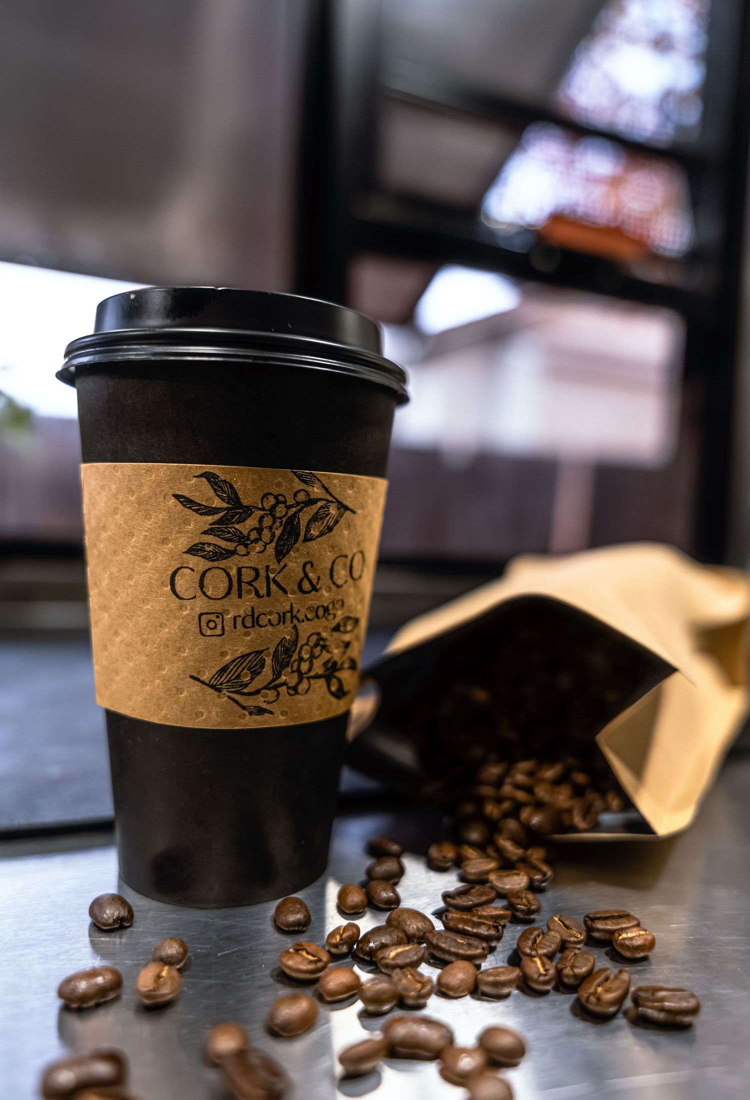 Coffee beans scattered around a black paper cup with a cork sleeve displaying the Cork & Co logo and coffee shop branding.