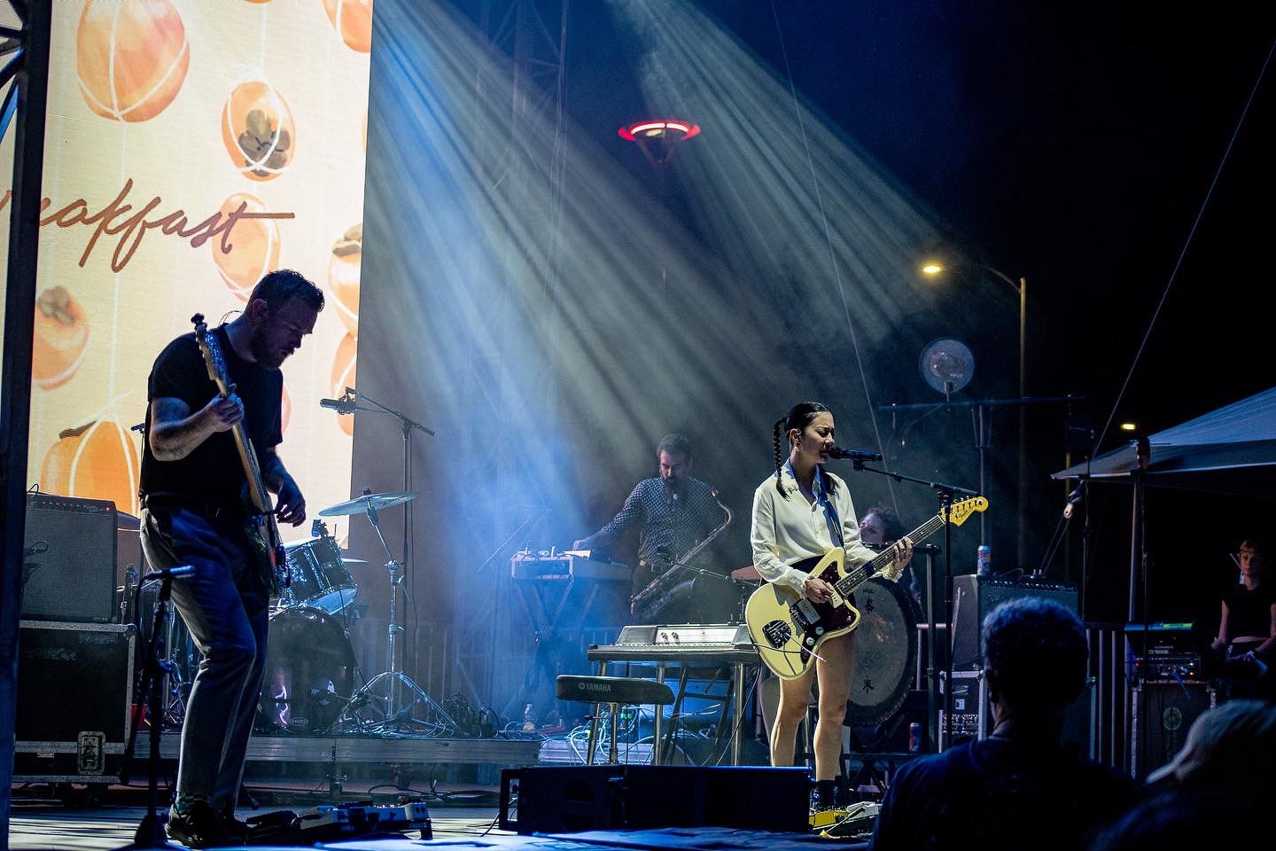 Wide concert stage view with dramatic spotlights and band performing live.