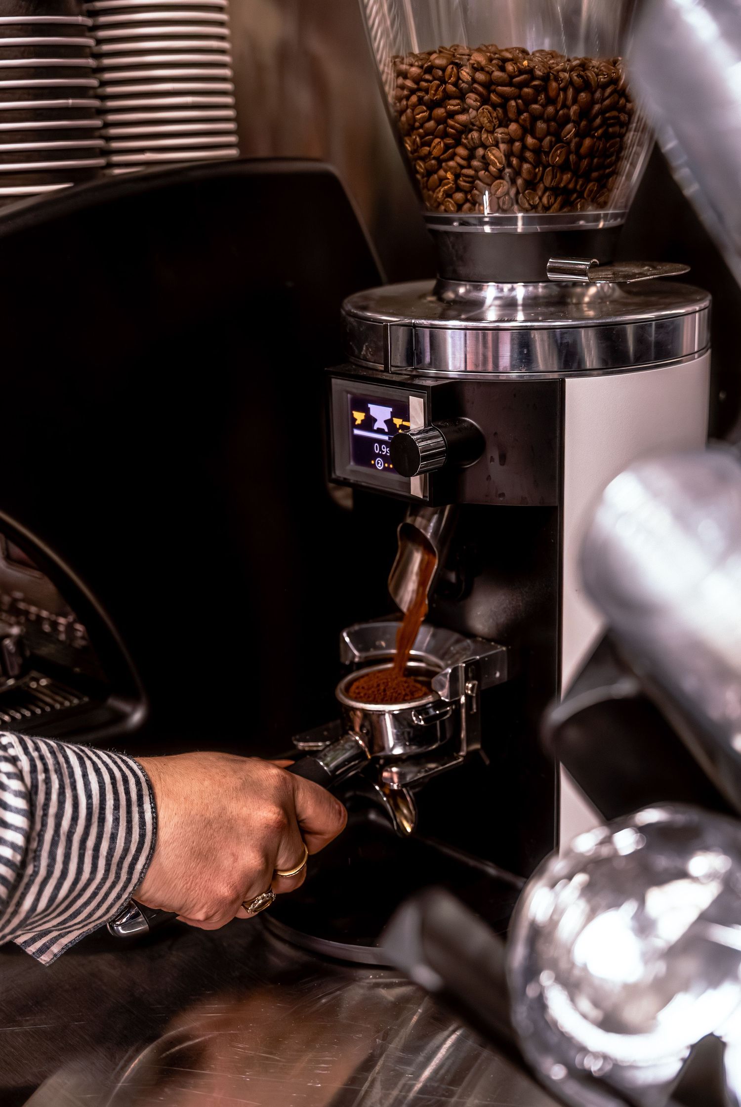 A barista in striped clothing preparing coffee with a professional espresso machine and roasted coffee beans.