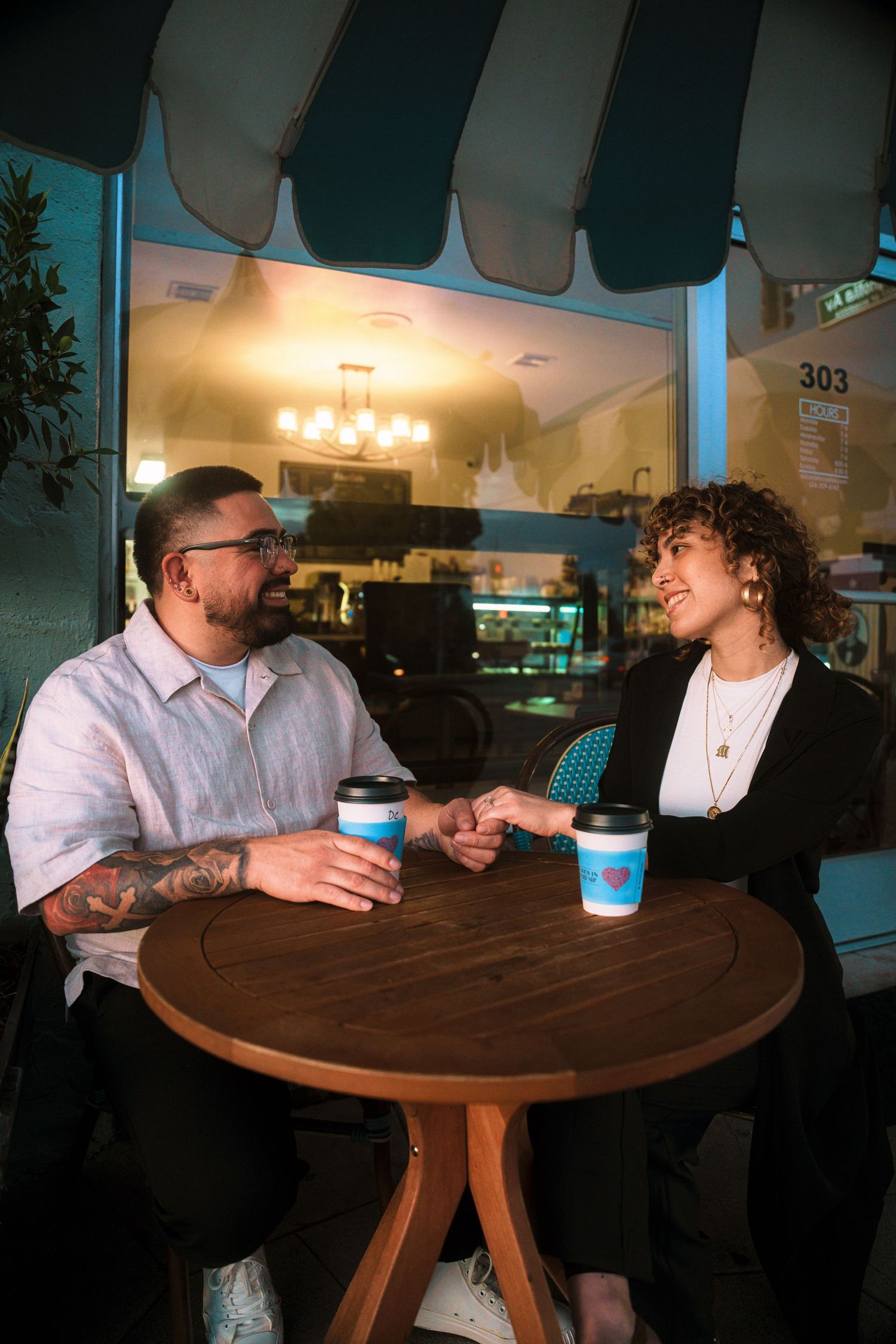 A couple having coffee and conversation at a round wooden table in a cafe.