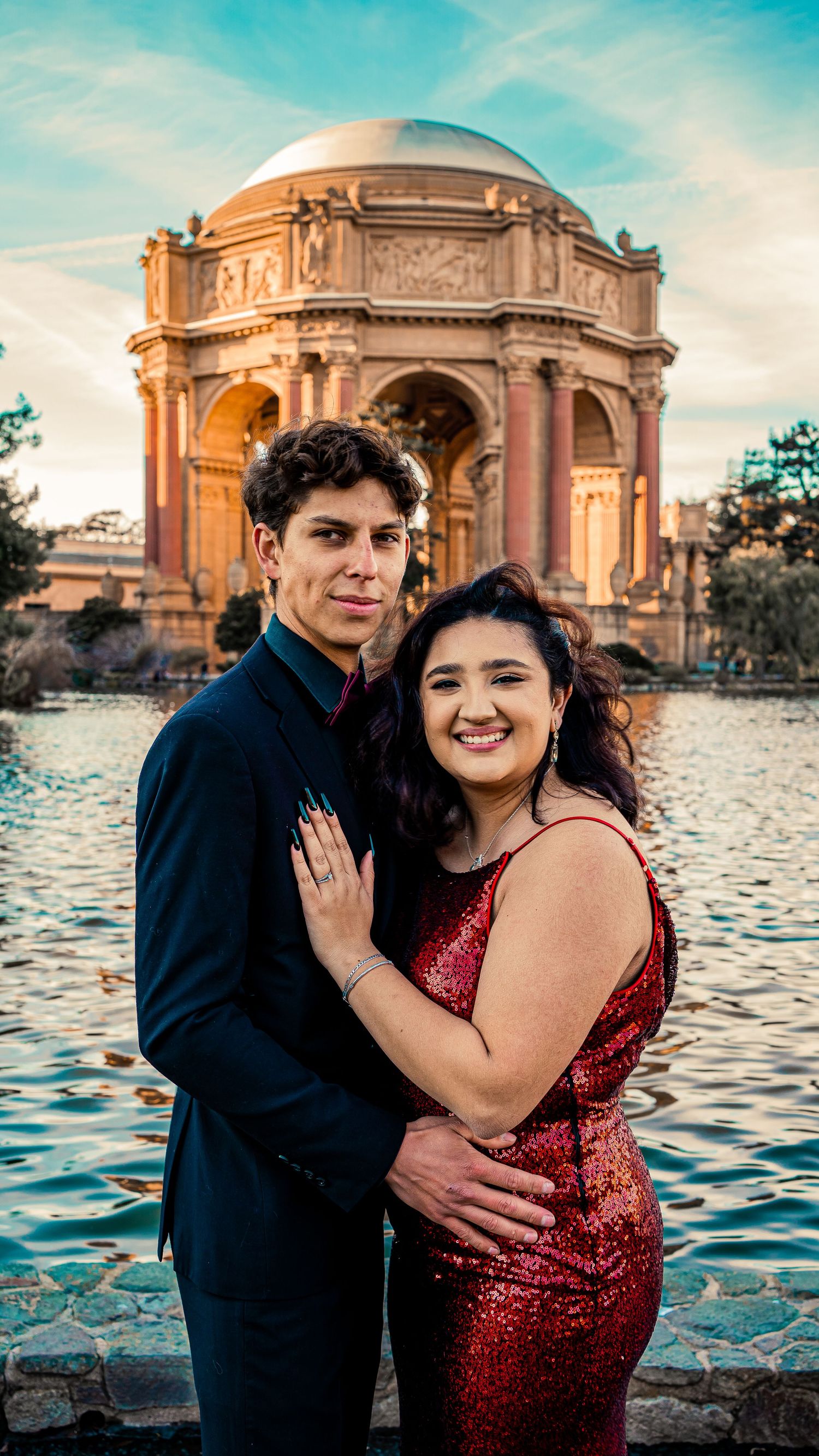 Happy couple embracing near the Palace of Fine Arts with water reflection in background.
