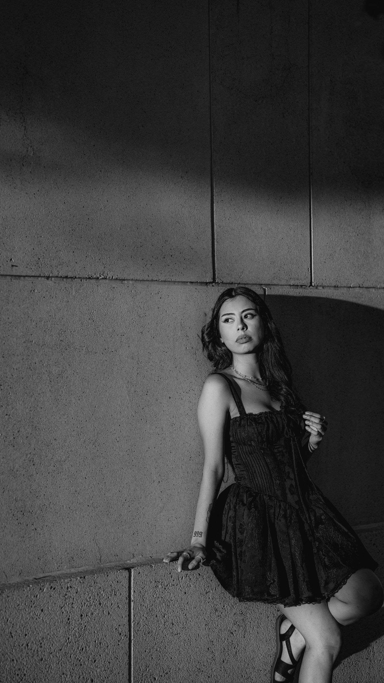 A black and white artistic photo series showing a figure in a dark dress against a concrete wall.