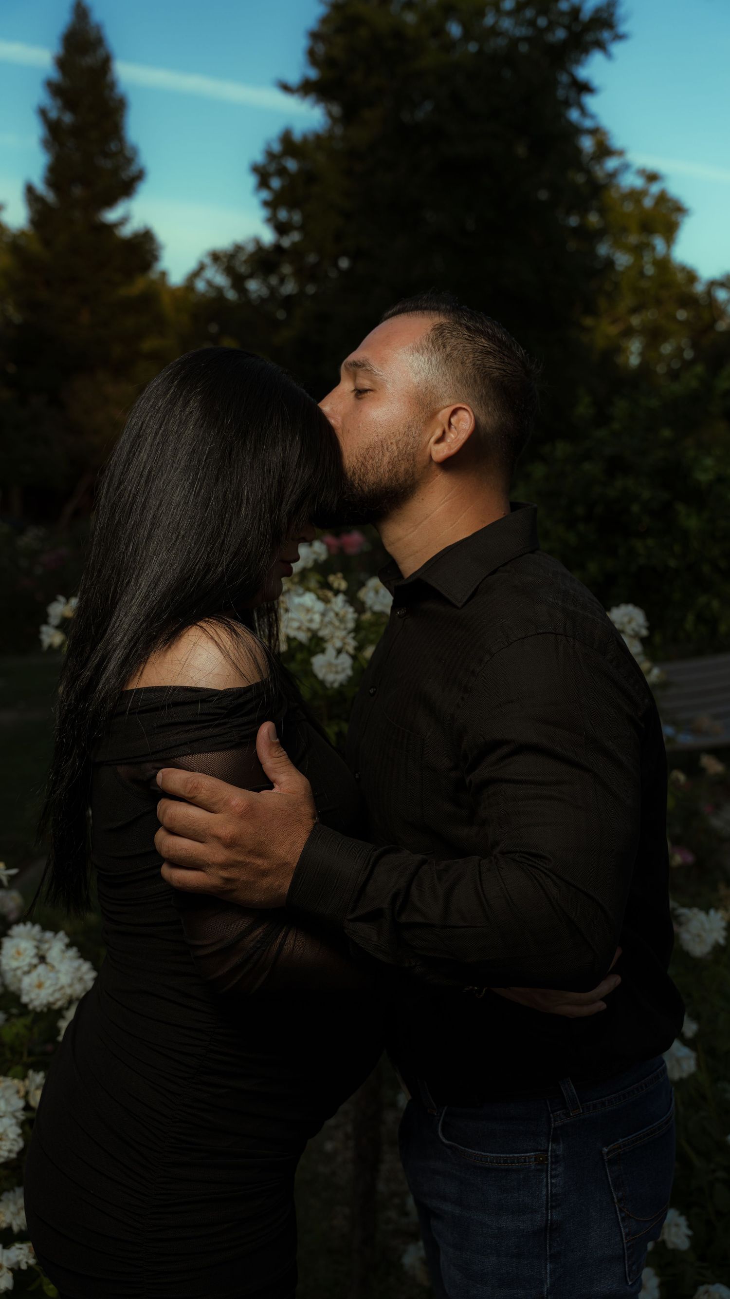 A romantic embrace captured at dusk with trees in the background.