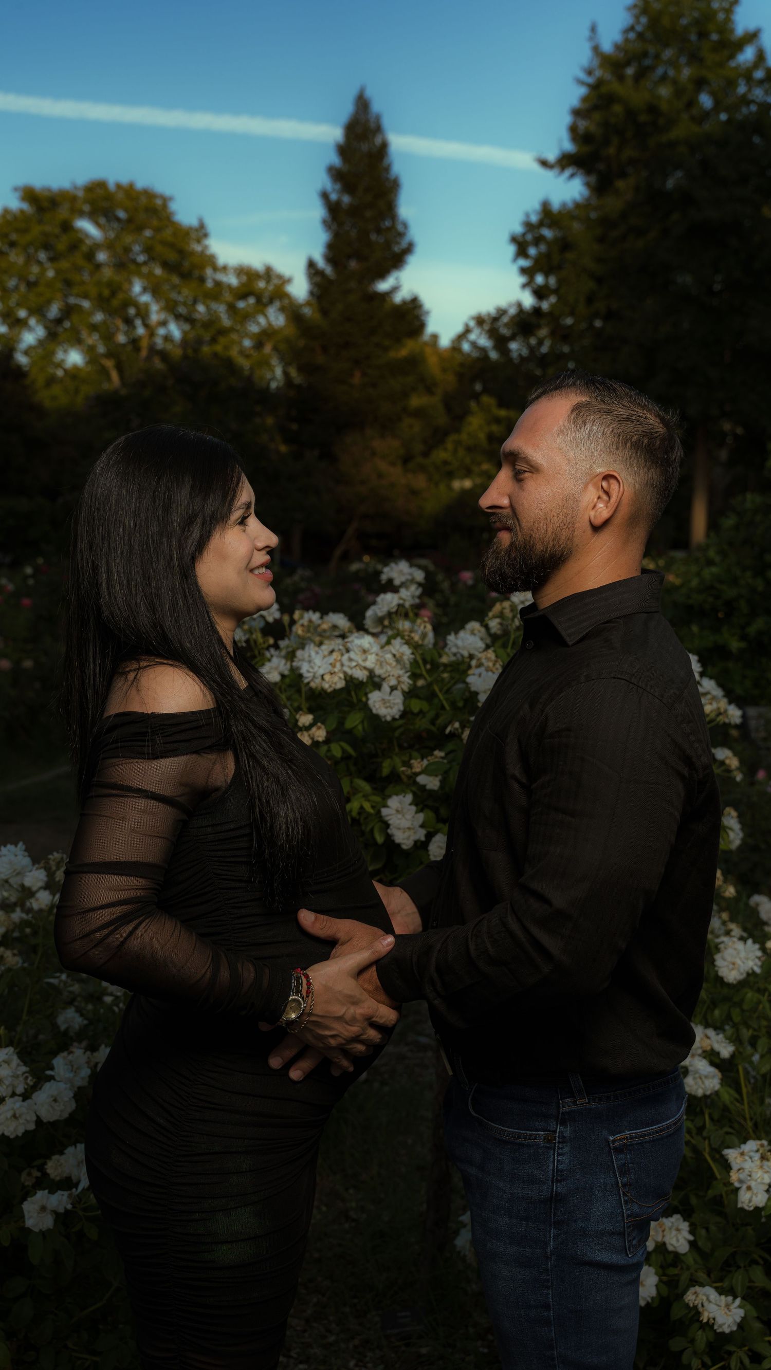 Couple shares romantic moment in garden with white flowers at dusk.