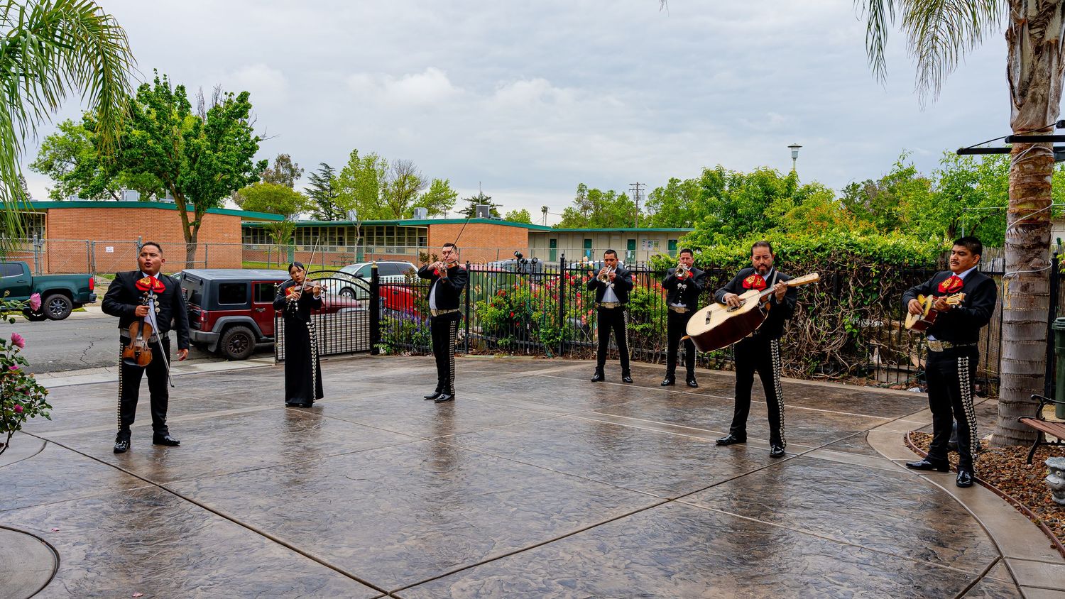 Panoramic view of a rainy outdoor celebration with palm trees and guests gathered under cloudy skies.